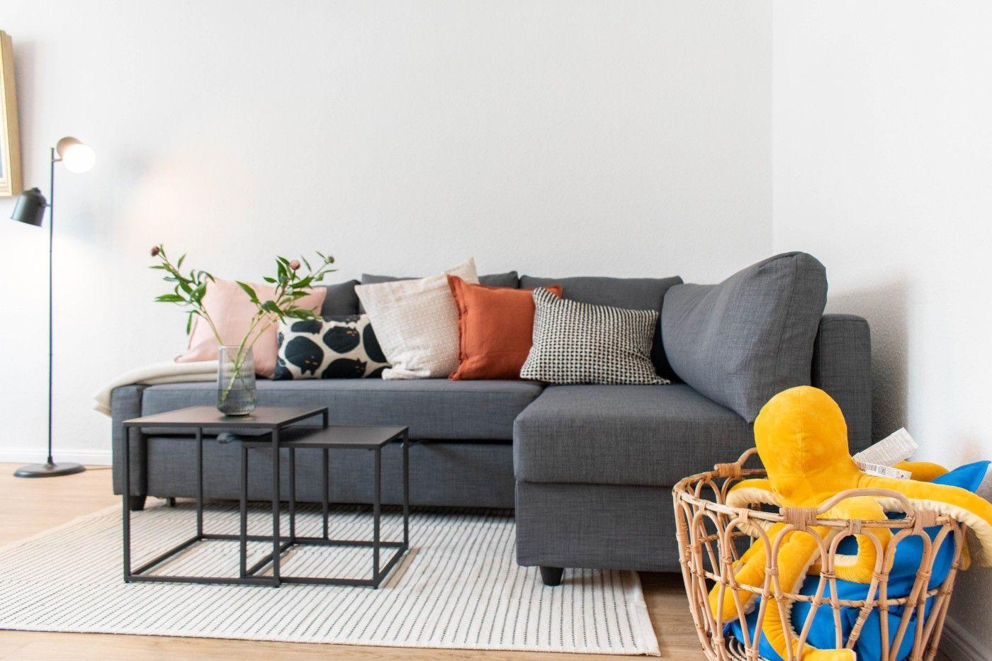 Ein grauer Sofa mit Kissen, zwei Tische und ein Korb mit Spielzeug.