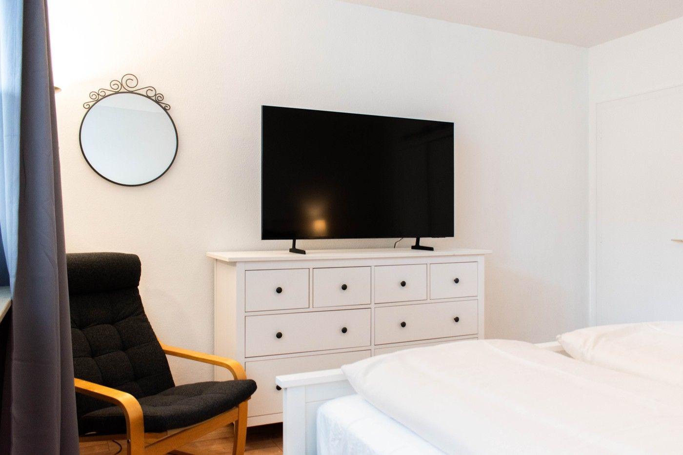 Schlafzimmer mit Bett, TV auf Schrank und schwarzer Sessel.