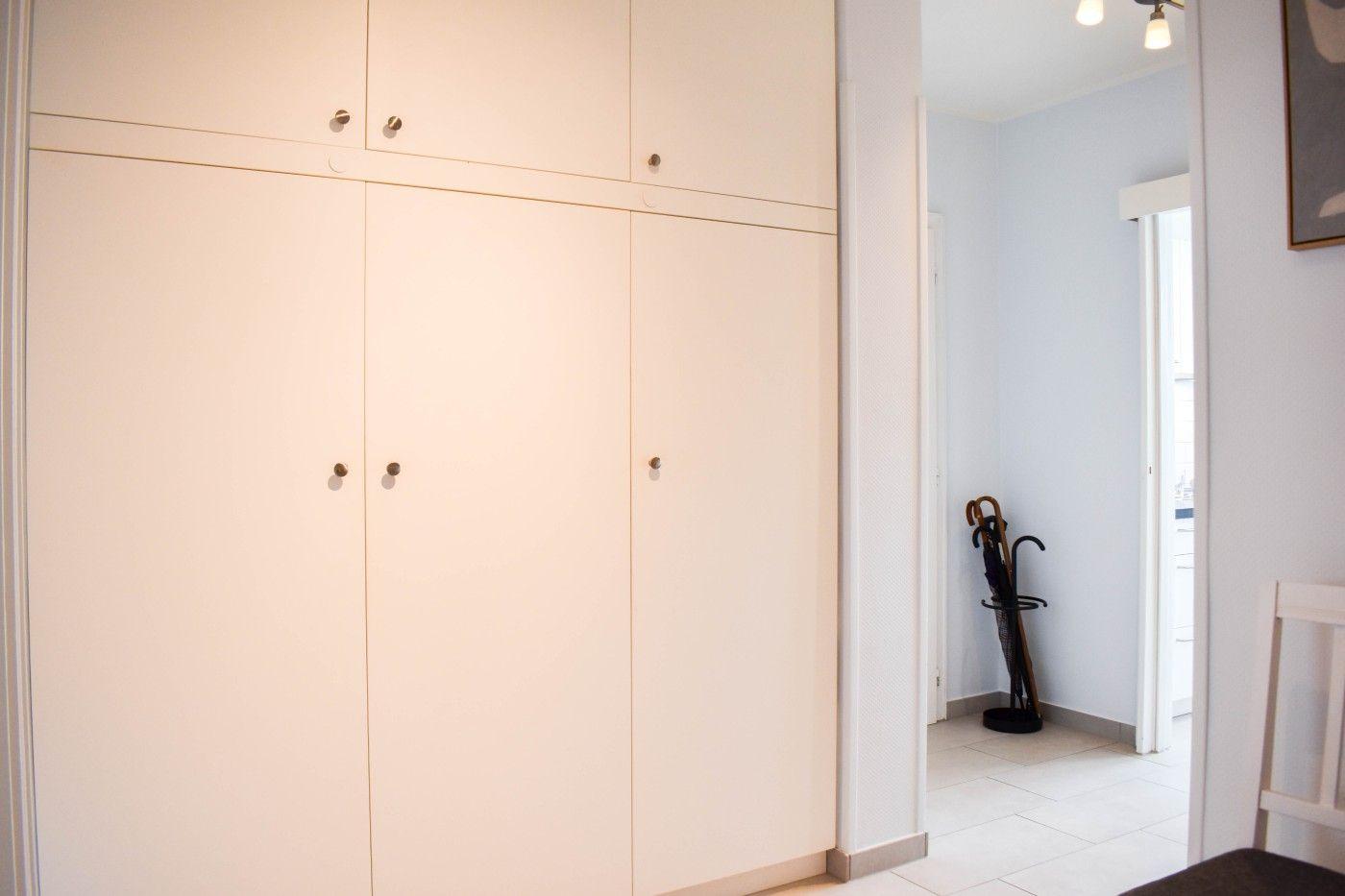 Großer Kleiderschrank mit drei Türen und zwei oberen Schubladen. Blick in einen Flur mit Regenschirmständer.