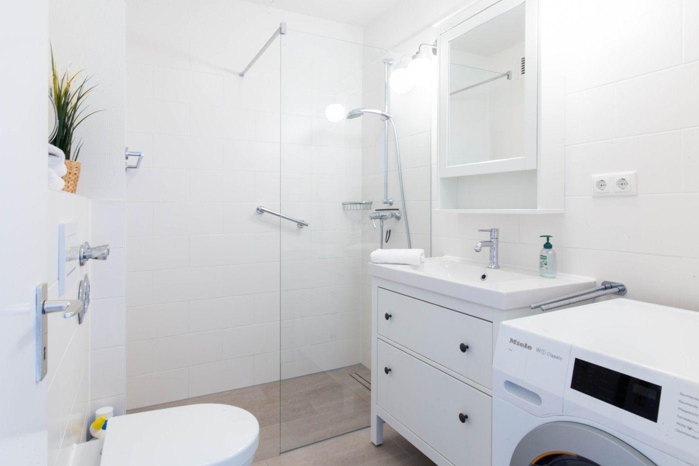 Badezimmer mit Dusche, Waschbecken und Waschmaschine.