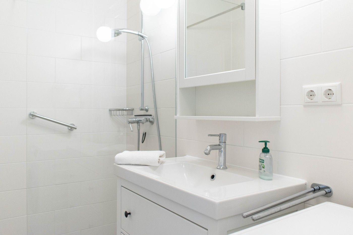 Badezimmer mit Dusche, Waschbecken und Spiegelschrank. Weiße Fliesen und moderne Armaturen.