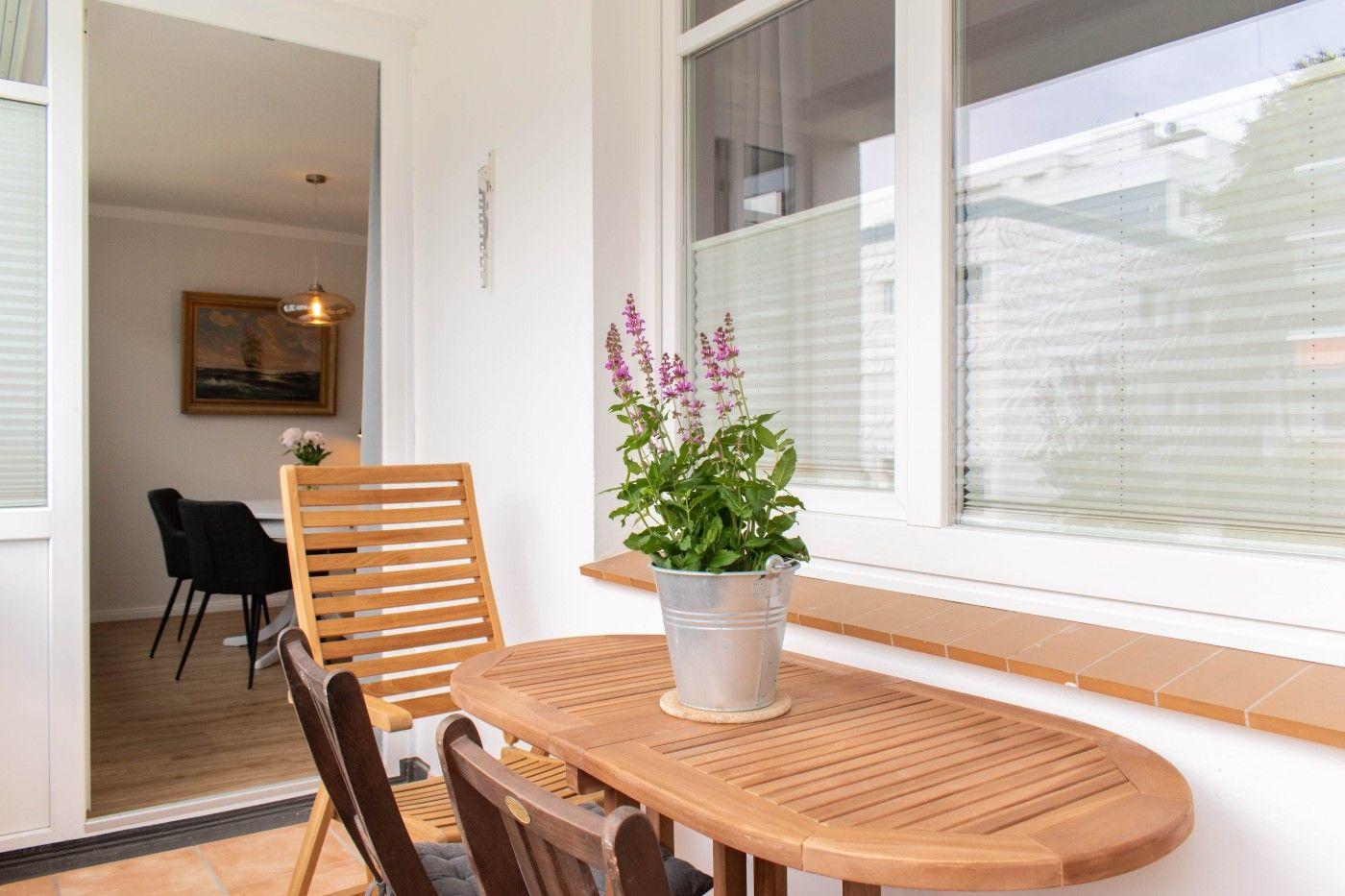 Terrasse mit Holztisch, Stühlen und Blumenkübel. Blick in das Esszimmer.