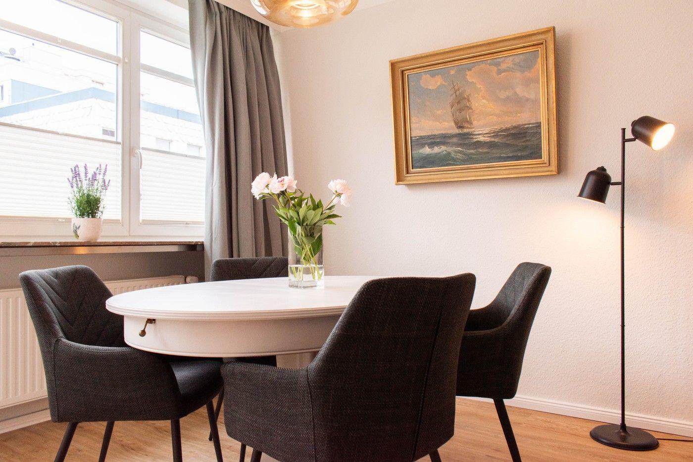 Rundtisch mit vier Stühlen, Wandbild und Stehlampe in einem Raum mit Fenster und Vorhängen.