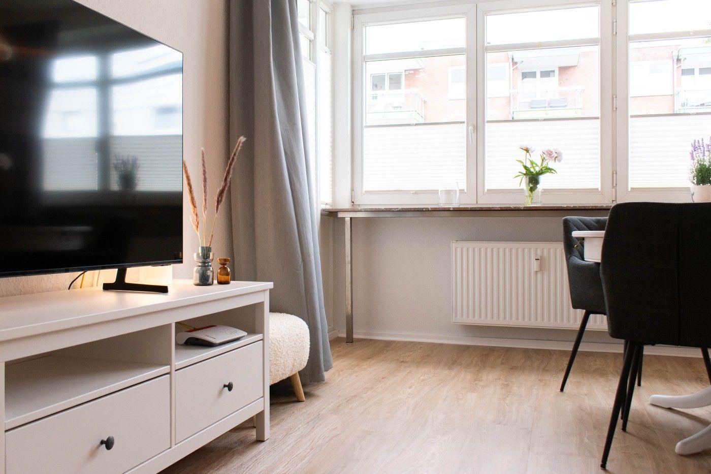 Wohnzimmer mit Fernseher, Fenster und Esstisch.