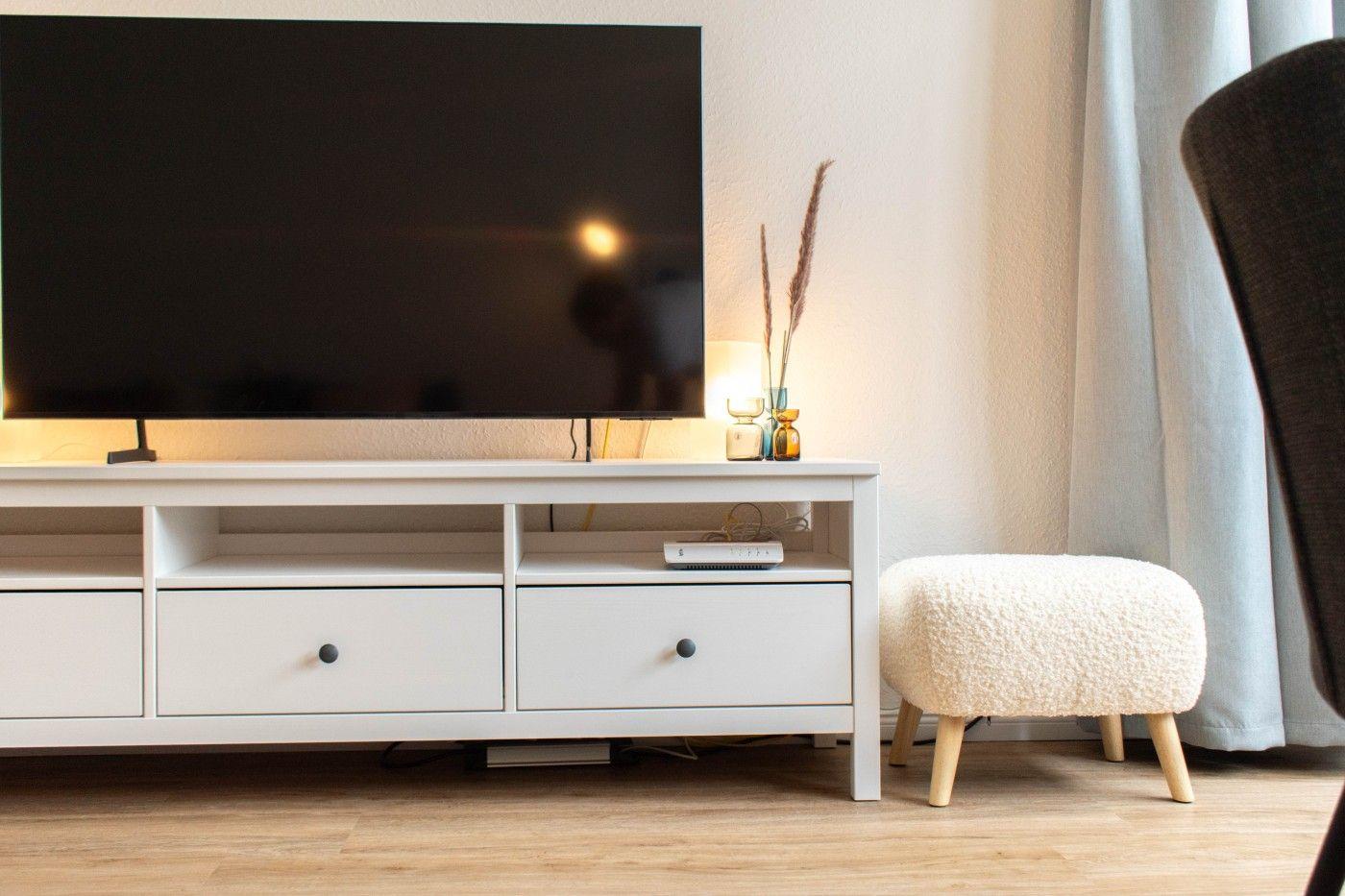 Flachbildfernseher auf weißen Schrank mit Schubladen und Stuhl daneben.