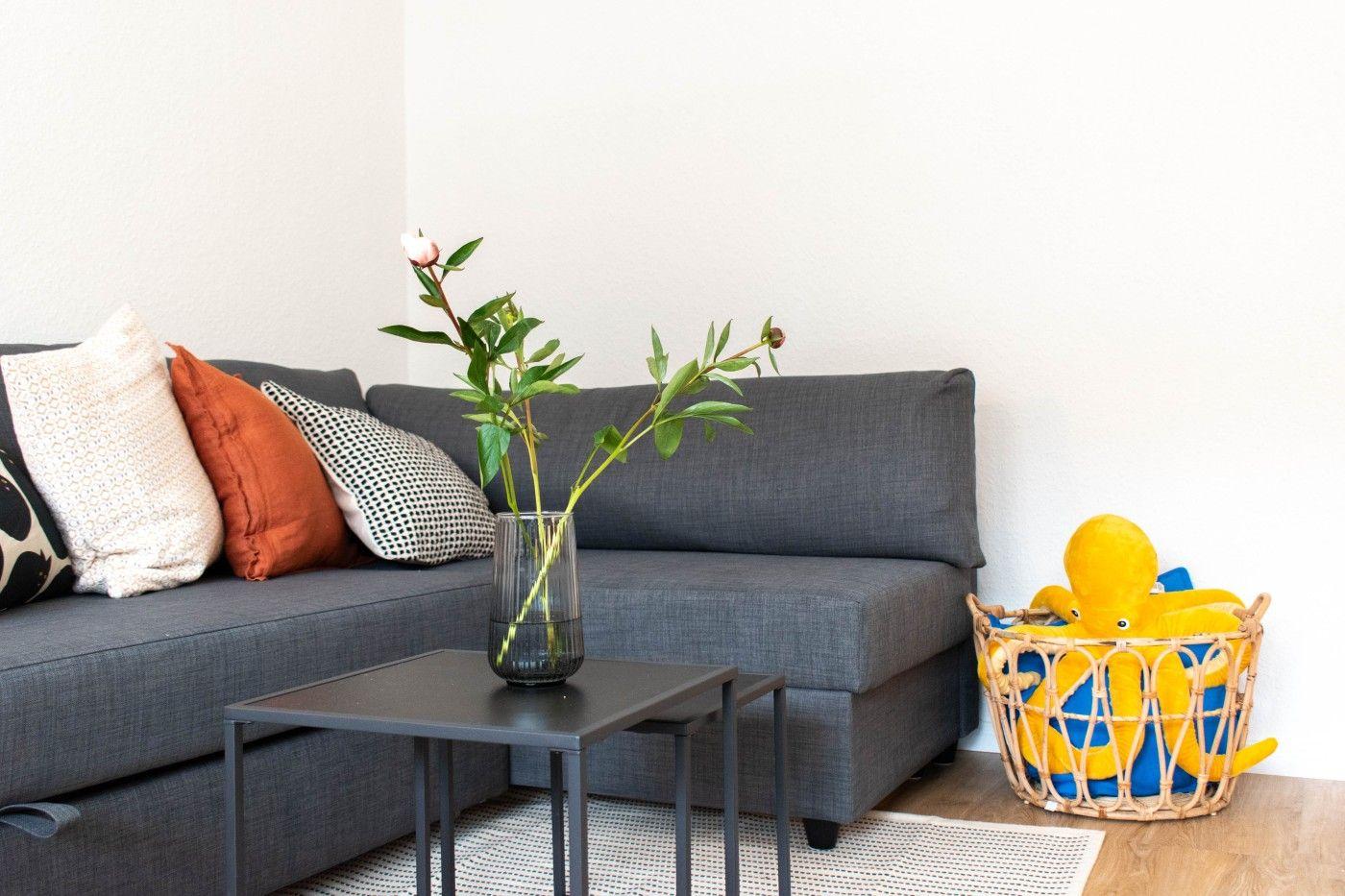 Grauer Sofa mit Kissen, Tisch mit Blumen und Korb mit Spielzeug.