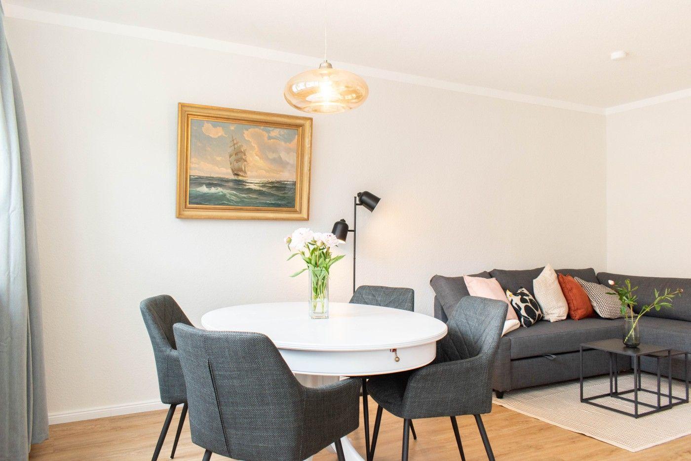 Essbereich mit runder Tisch und vier Stühlen. Wohnbereich mit Sofa und Kissen.
