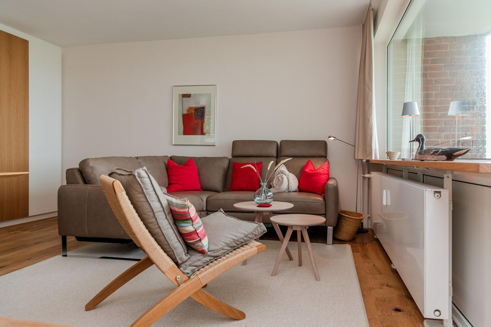 Ein Wohnzimmer mit braunem Sofa, roten Kissen und einem Holzstuhl.