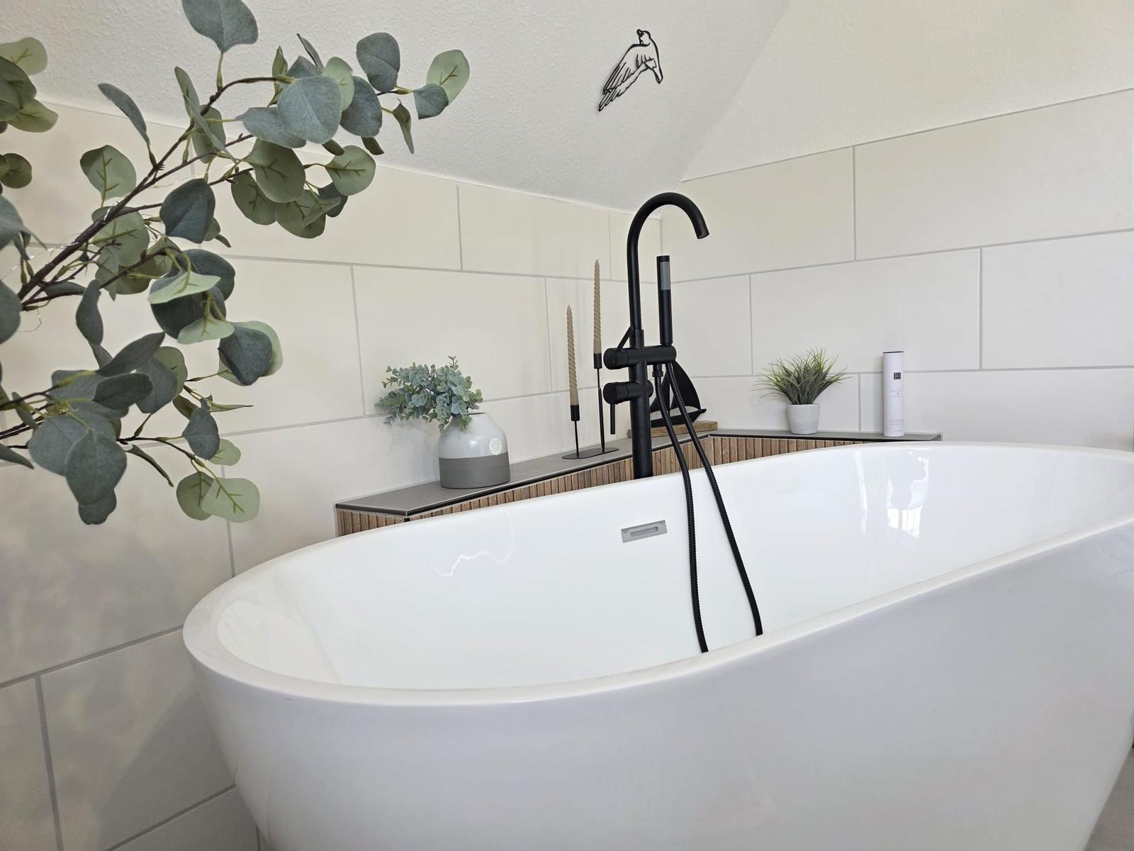 Freistehende Badewanne mit schwarzer Armatur und Pflanzen im Badezimmer.