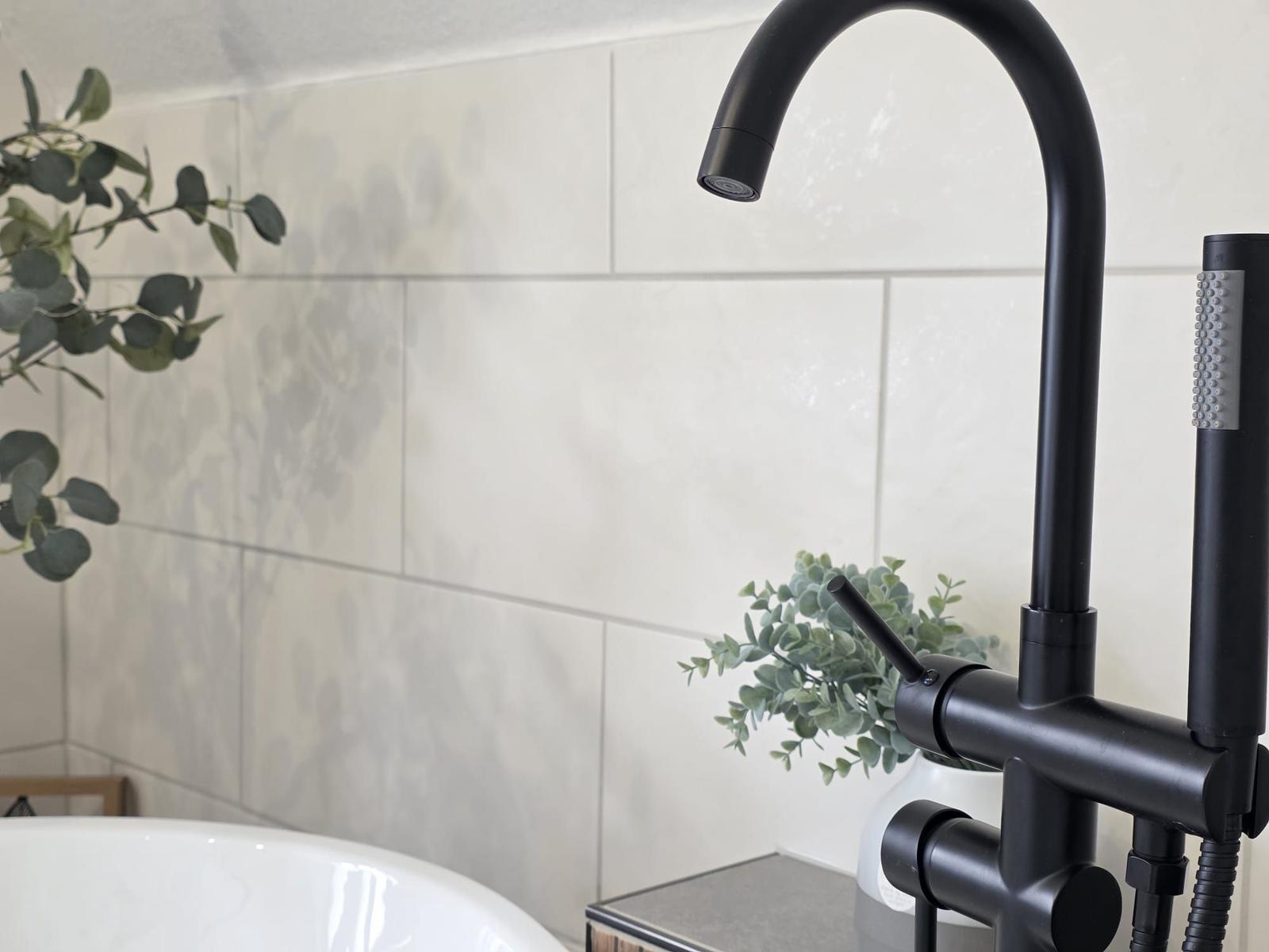 Duschkopf und Handbrause über Badewanne mit Pflanzen und Fliesenwand.