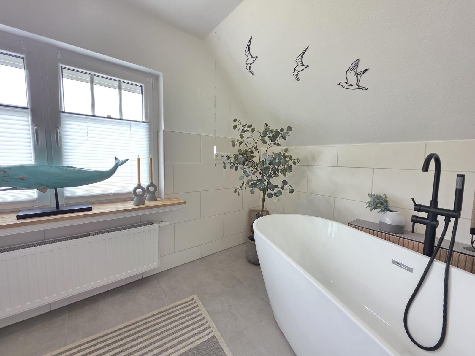 Bad mit freistehender Badewanne, Fenster, Wanddekoration und Pflanzen.