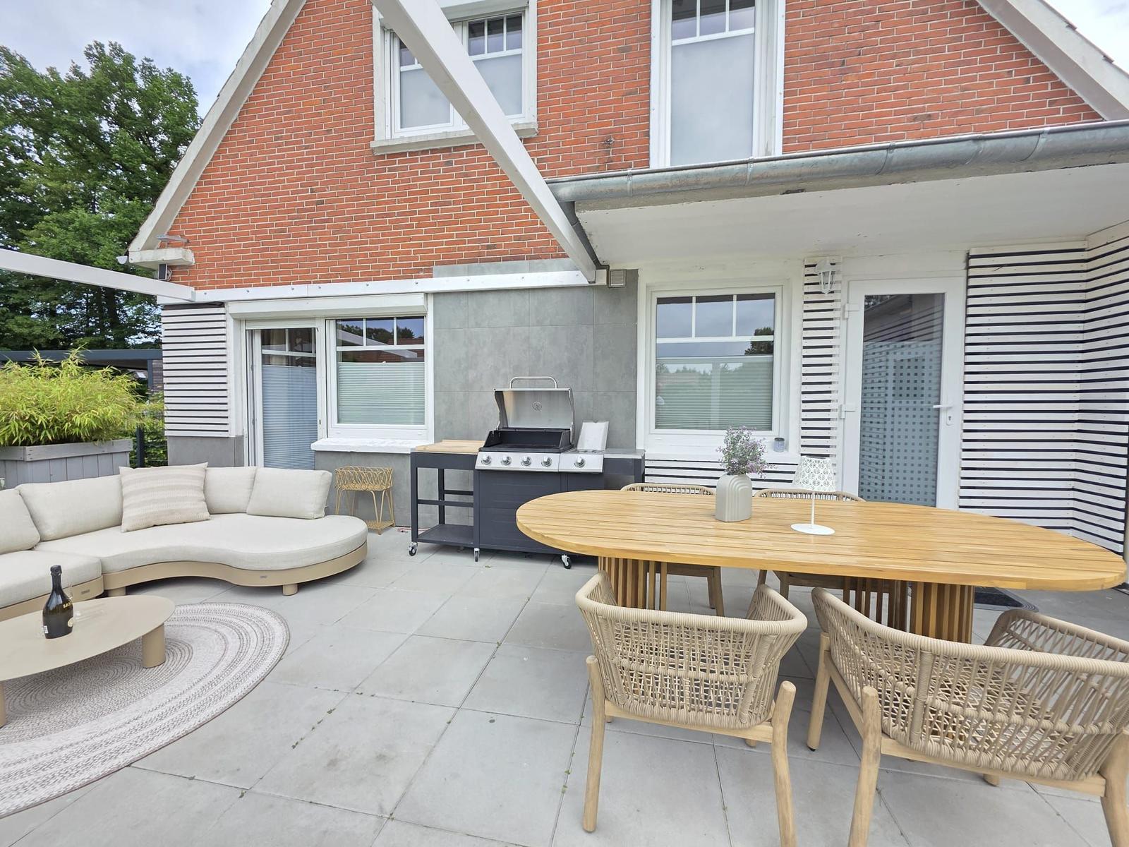 Terrasse mit Sitzgruppe, Esstisch und Grill. Modernes Design mit Holz- und Stoffmöbeln.