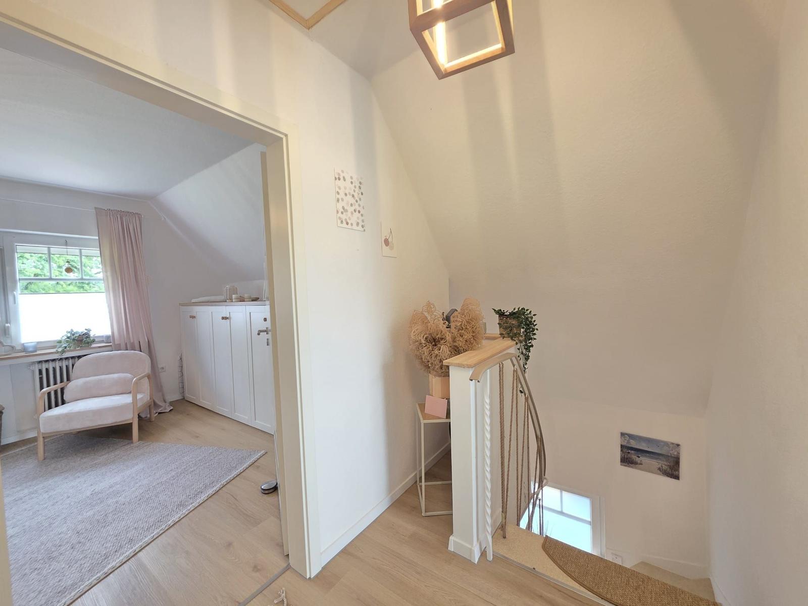 Haus mit Treppe und Blick in Wohnbereich mit Stuhl und Gardinen.