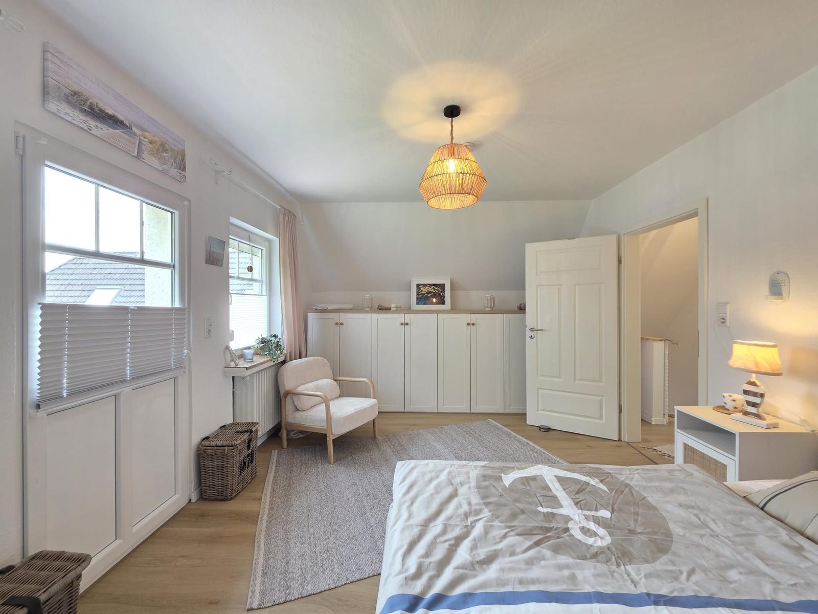Schlafzimmer mit Bett, Nachttisch, Stuhl und Fenster. Deckenleuchte und Schrank sind sichtbar.