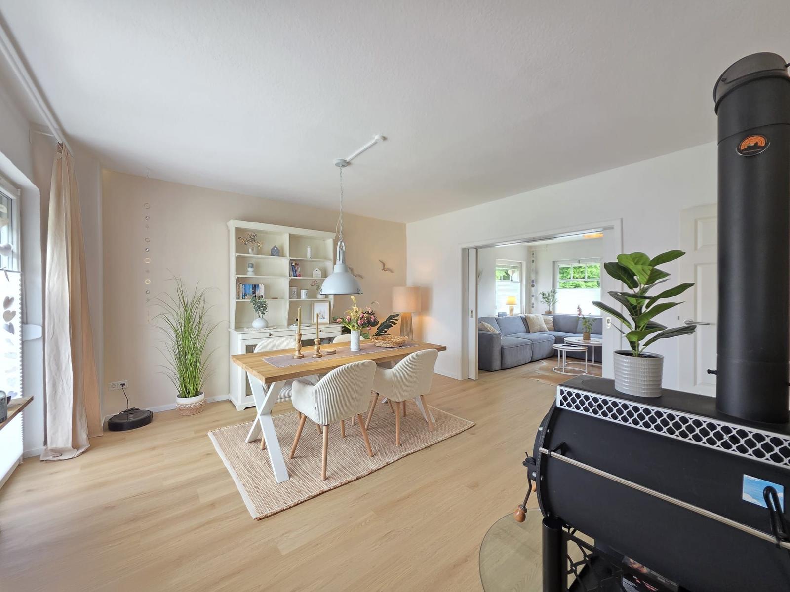Essbereich mit Tisch, Stühlen und Bücherregal. Wohnzimmer mit Sofa und Kamin im Hintergrund.