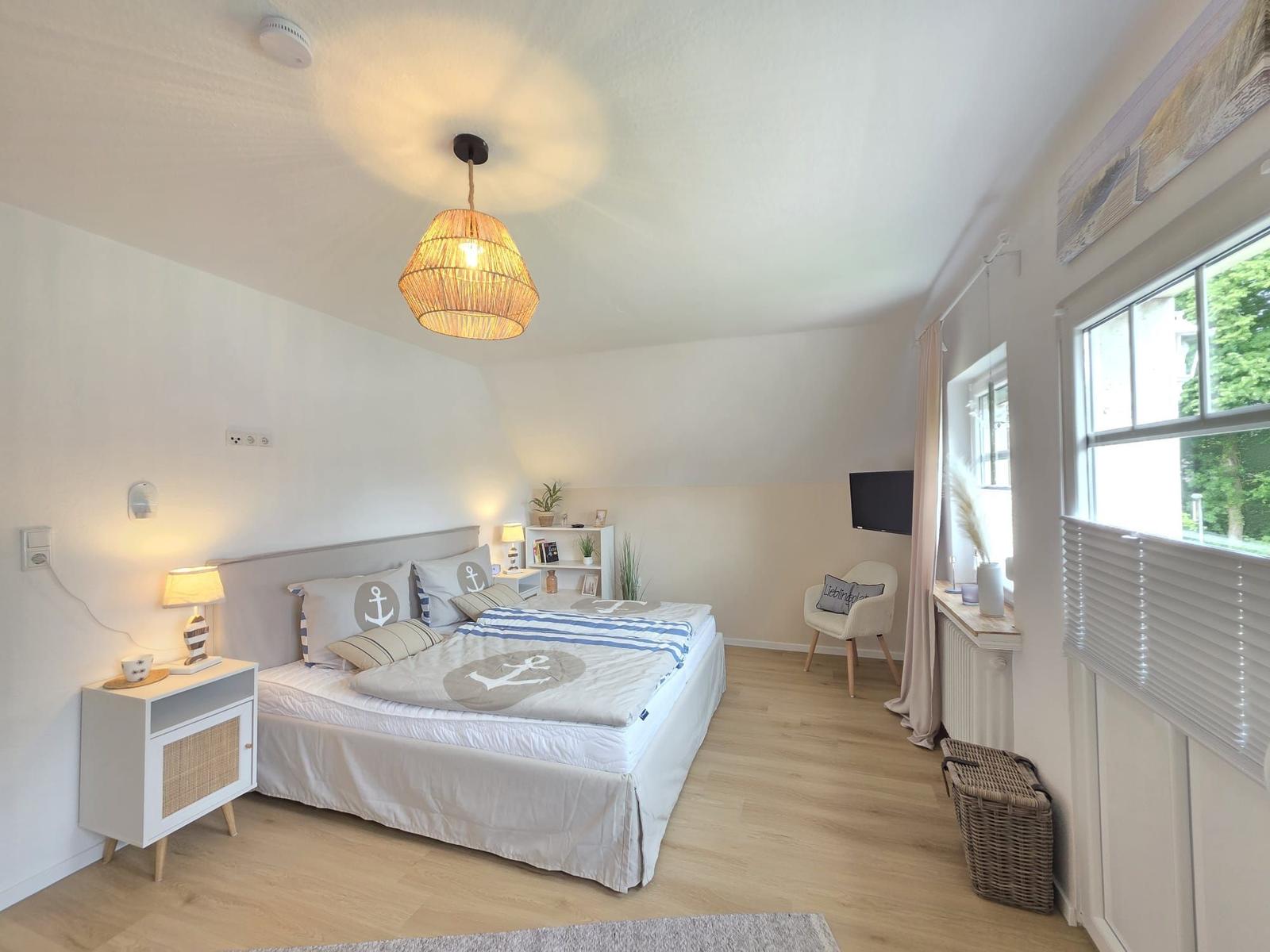 Schlafzimmer mit Bett, Nachttisch, Lampe und Fenster mit Jalousie.