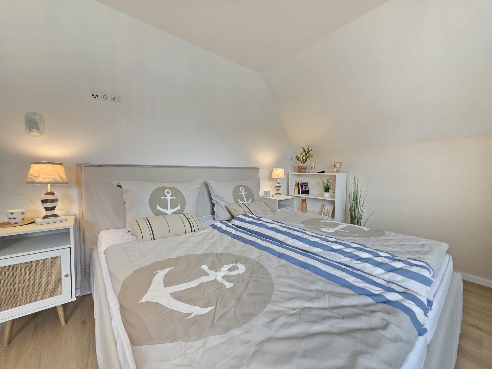 Schlafzimmer mit Bett, Nachttisch und Regal. Dekoration mit Ankern und Streifen.