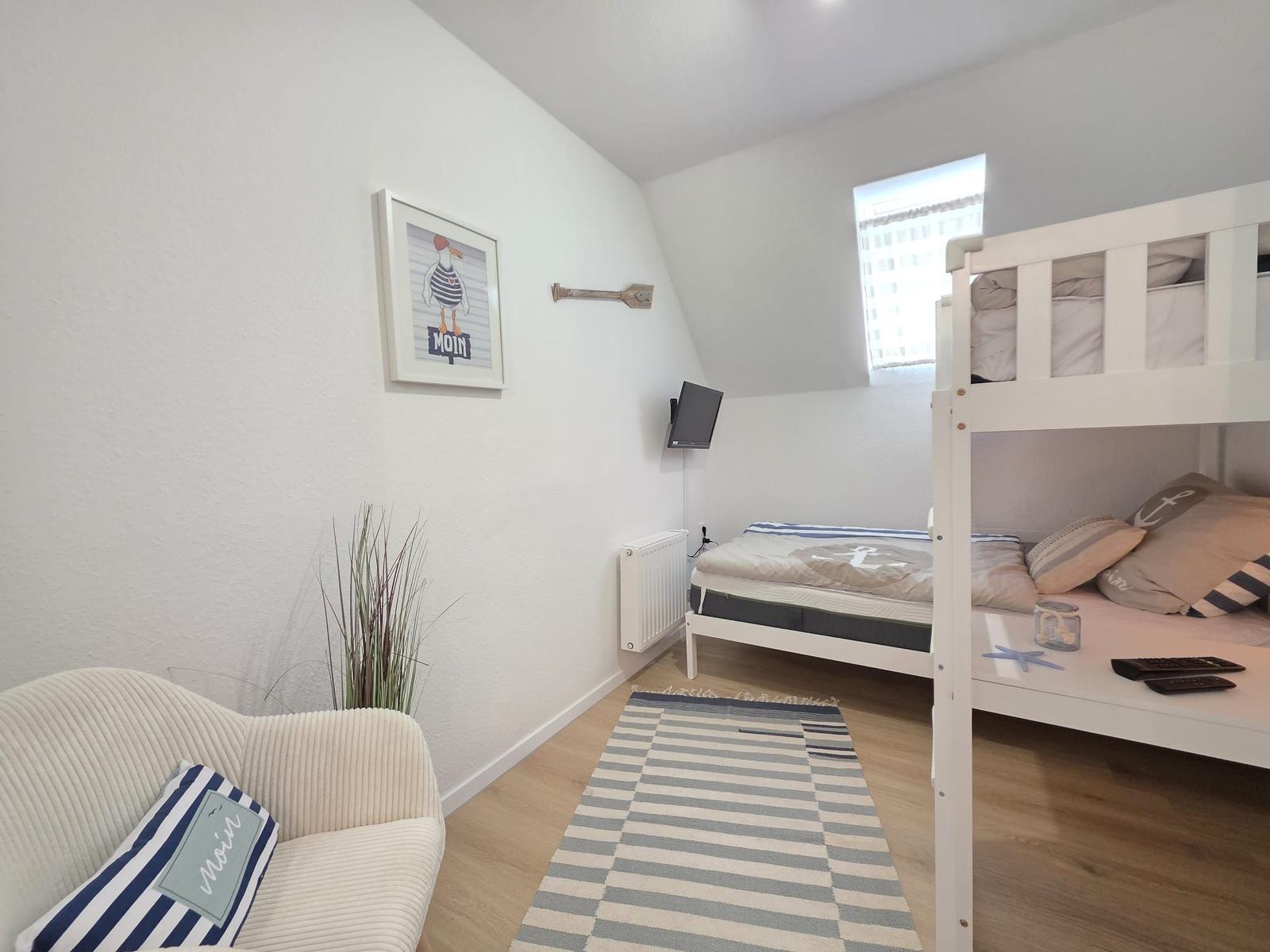 Schlafzimmer mit Doppelstockbett, Sessel und Wandbild. Holzdielenboden und Fenster.
