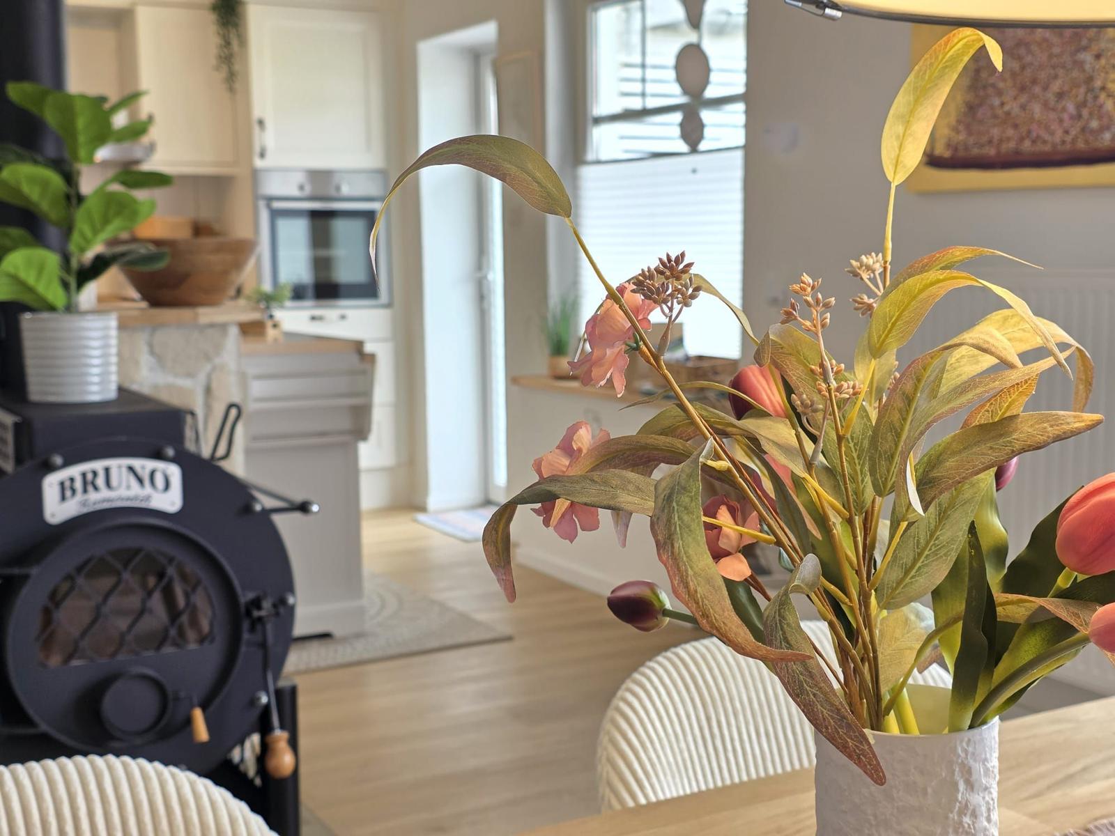 Ein Essbereich mit Blumenvase und Kaminofen im Hintergrund.