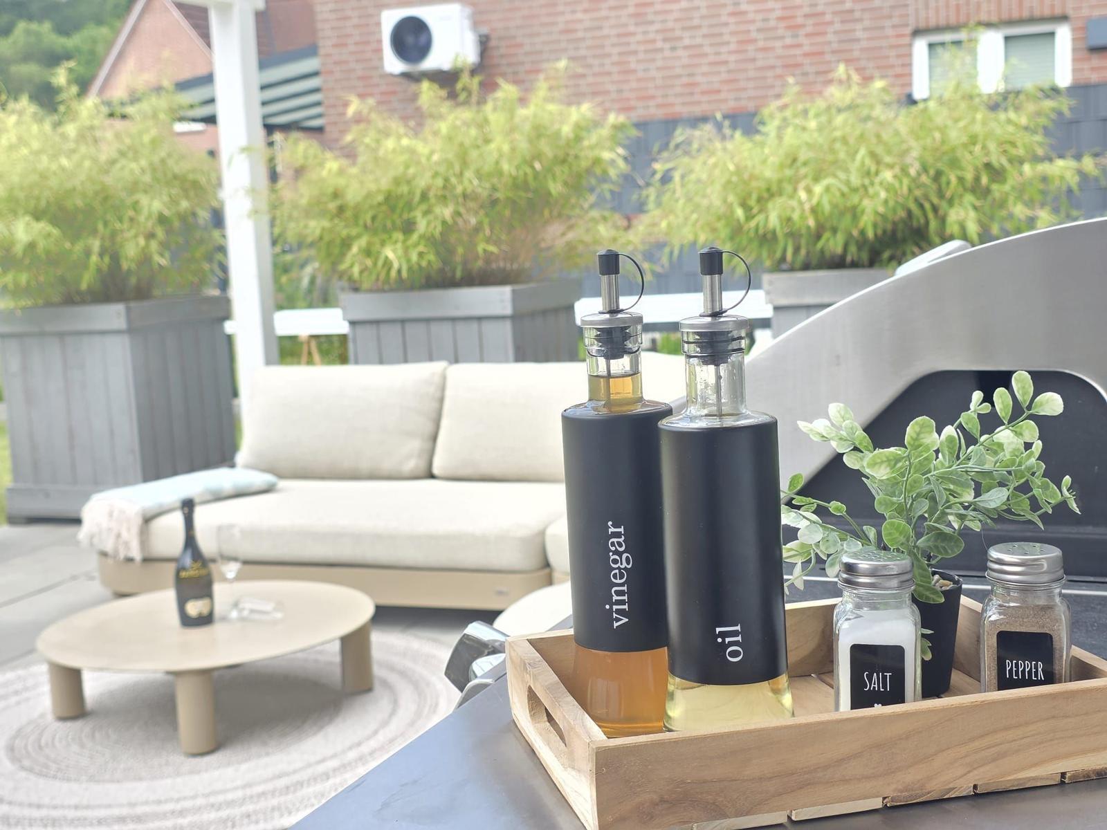 Auf der Terrasse stehen Öle und Essig in Flaschen mit Salz- und Pfefferstreuer.