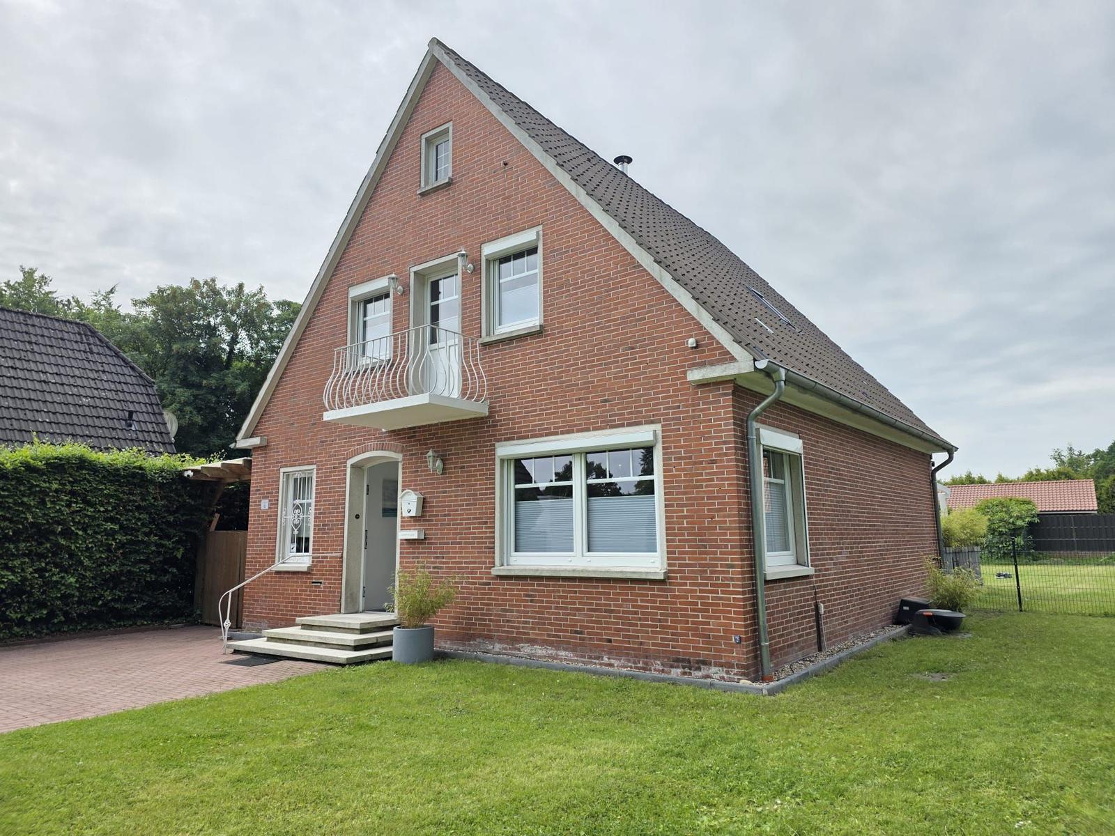 Zweistöckiges Haus mit Balkon, Eingangstreppe und Garten.