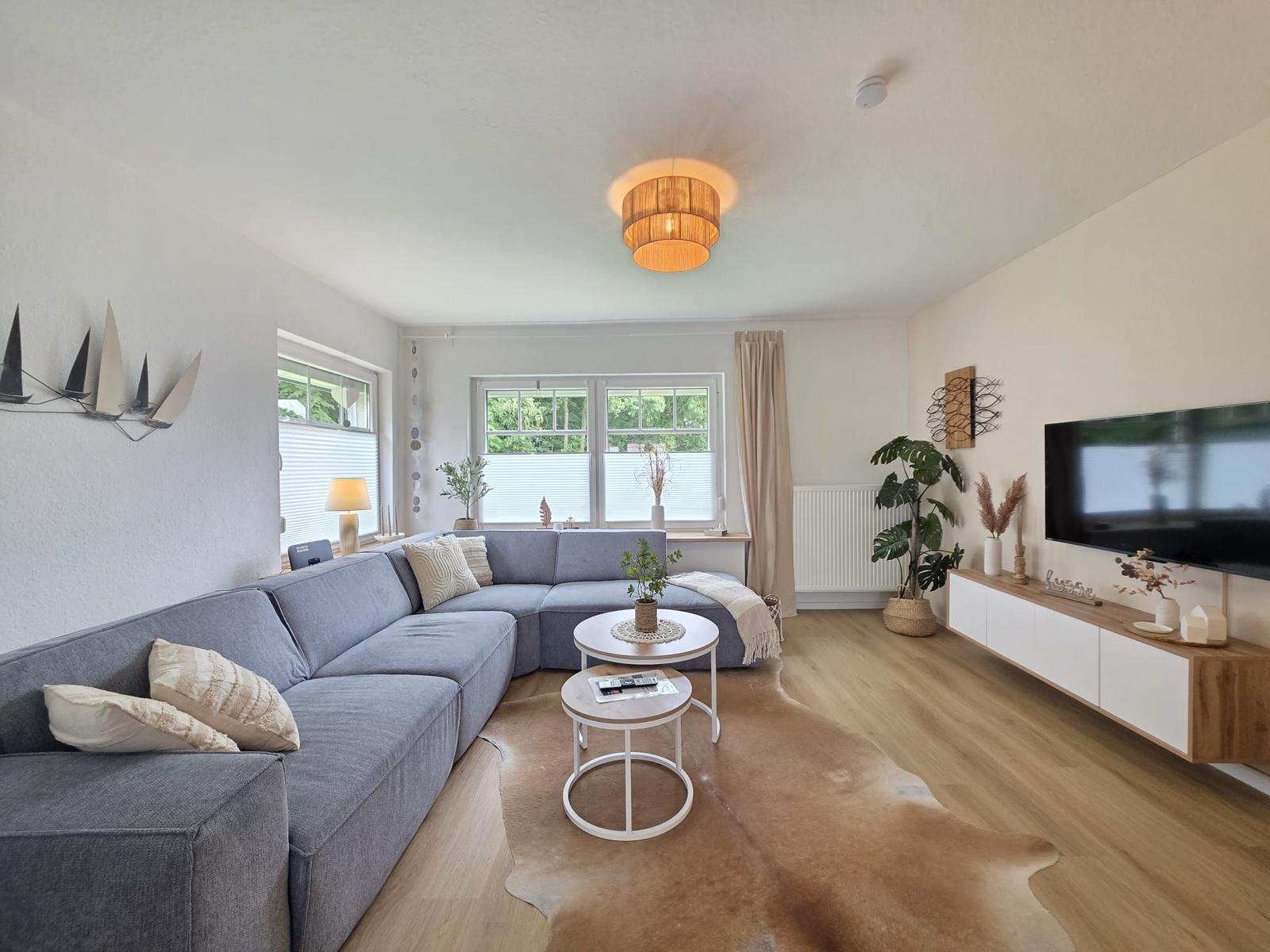 Wohnzimmer mit grauem Sofa, Holzboden und Fernseher an der Wand.