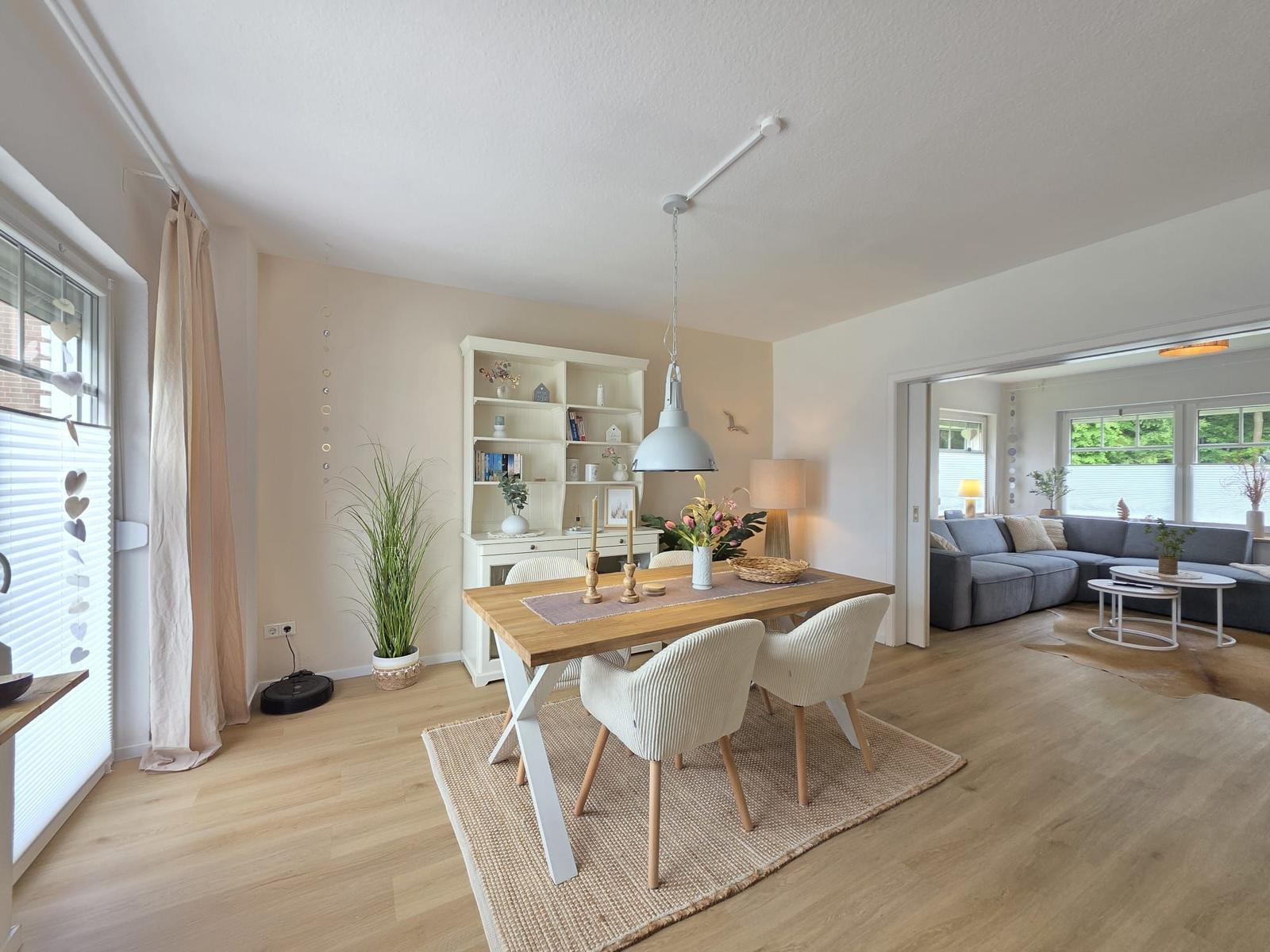 Essbereich mit Holztisch und Stühlen. Wohnzimmer mit Sofa und Fenstern.