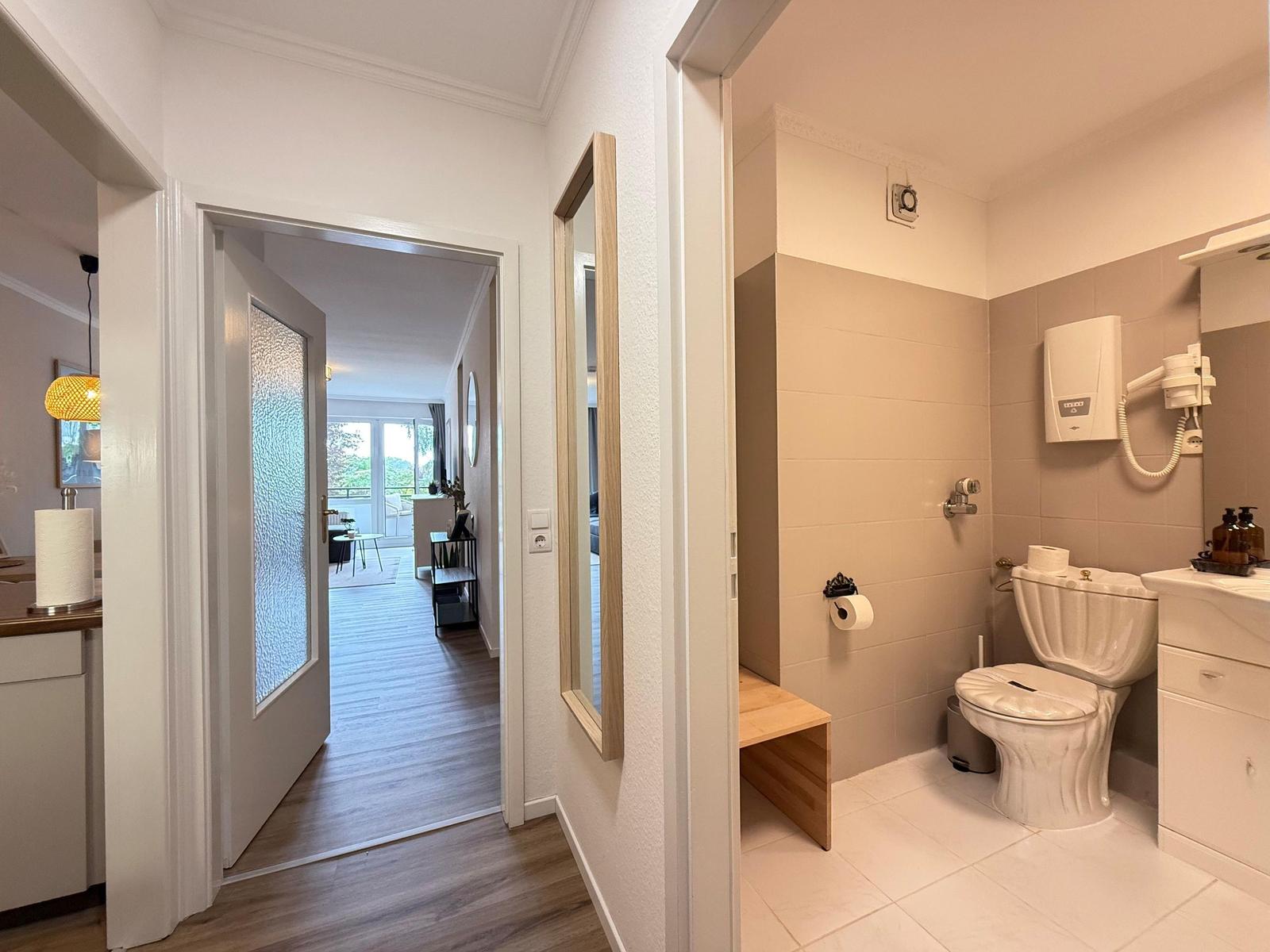 Badezimmer mit Toilette und Waschbecken. Durchgang zur Wohnung mit Holzboden.