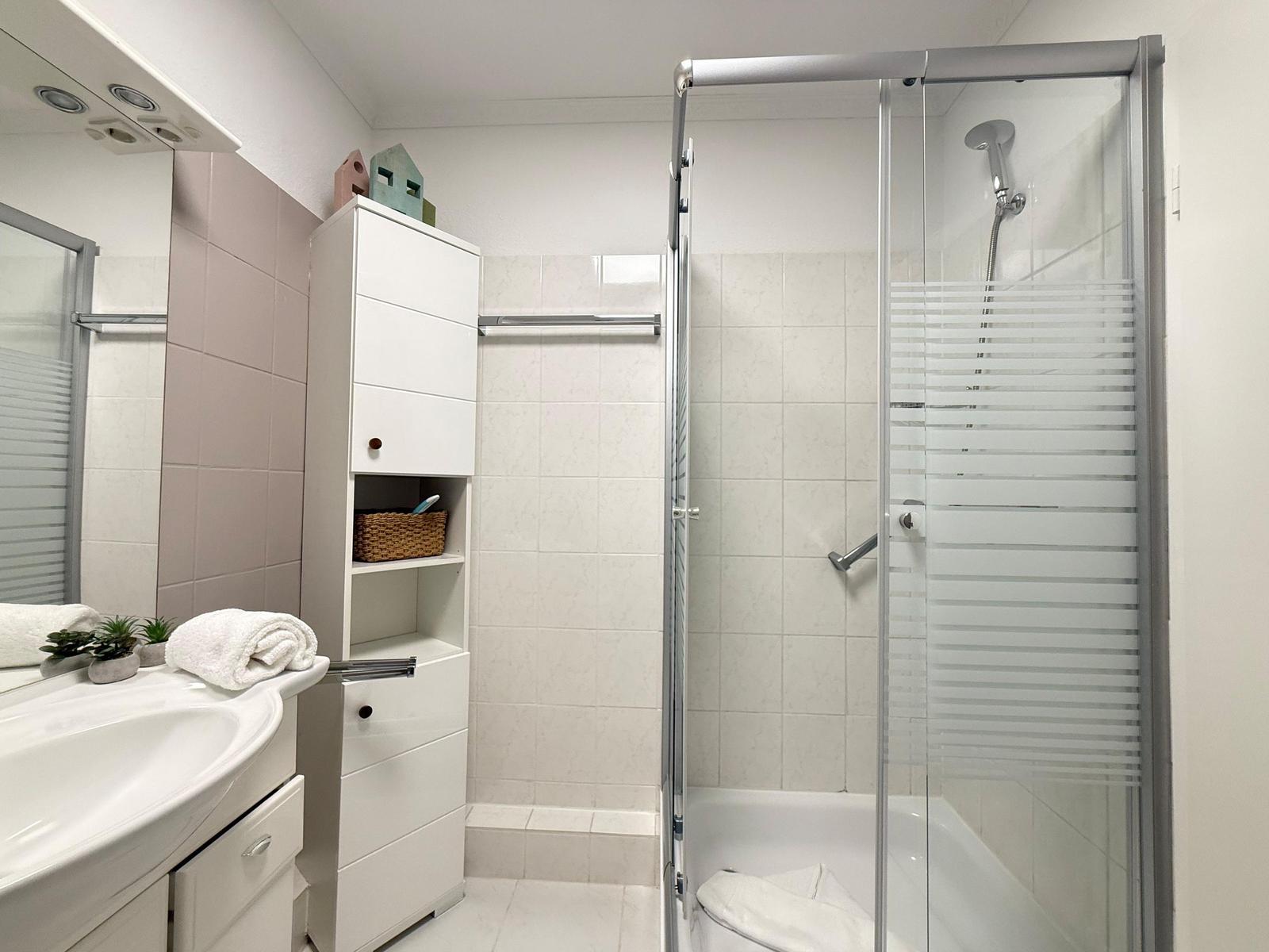 Badezimmer mit Dusche, Waschbecken und Aufbewahrungsmöbel.