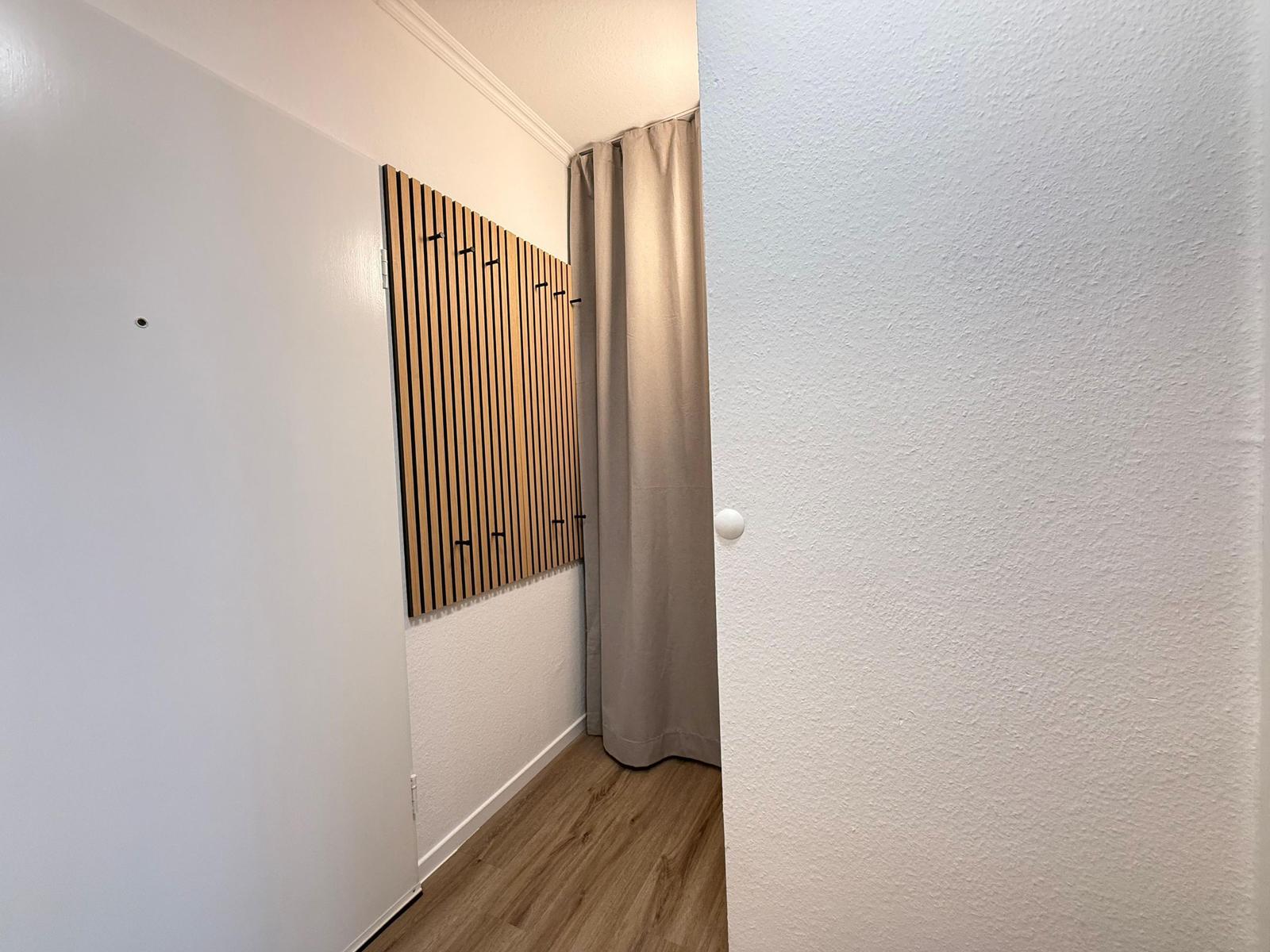 Flur mit Holzparkett, weißen Wänden und Holzgarderobe mit Haken.