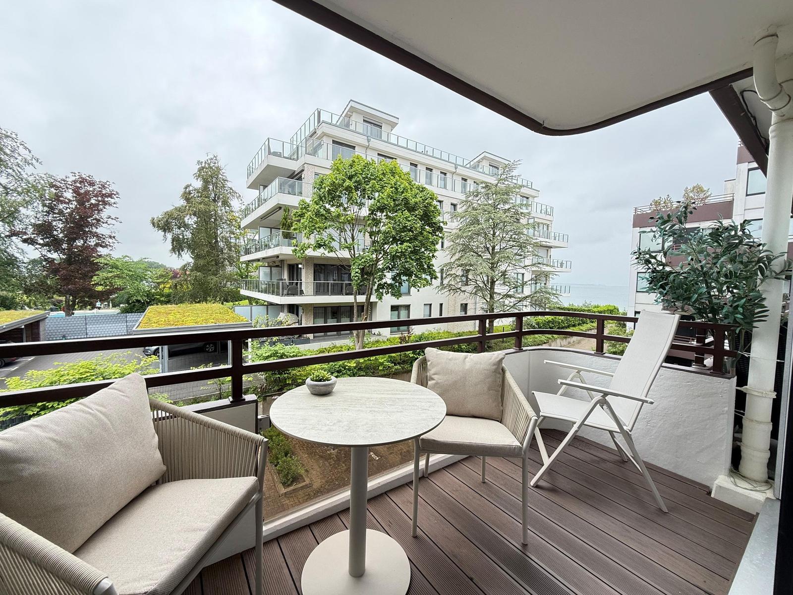 Terrasse mit Tisch und Stühlen, Blick auf Gebäude und Bäume.