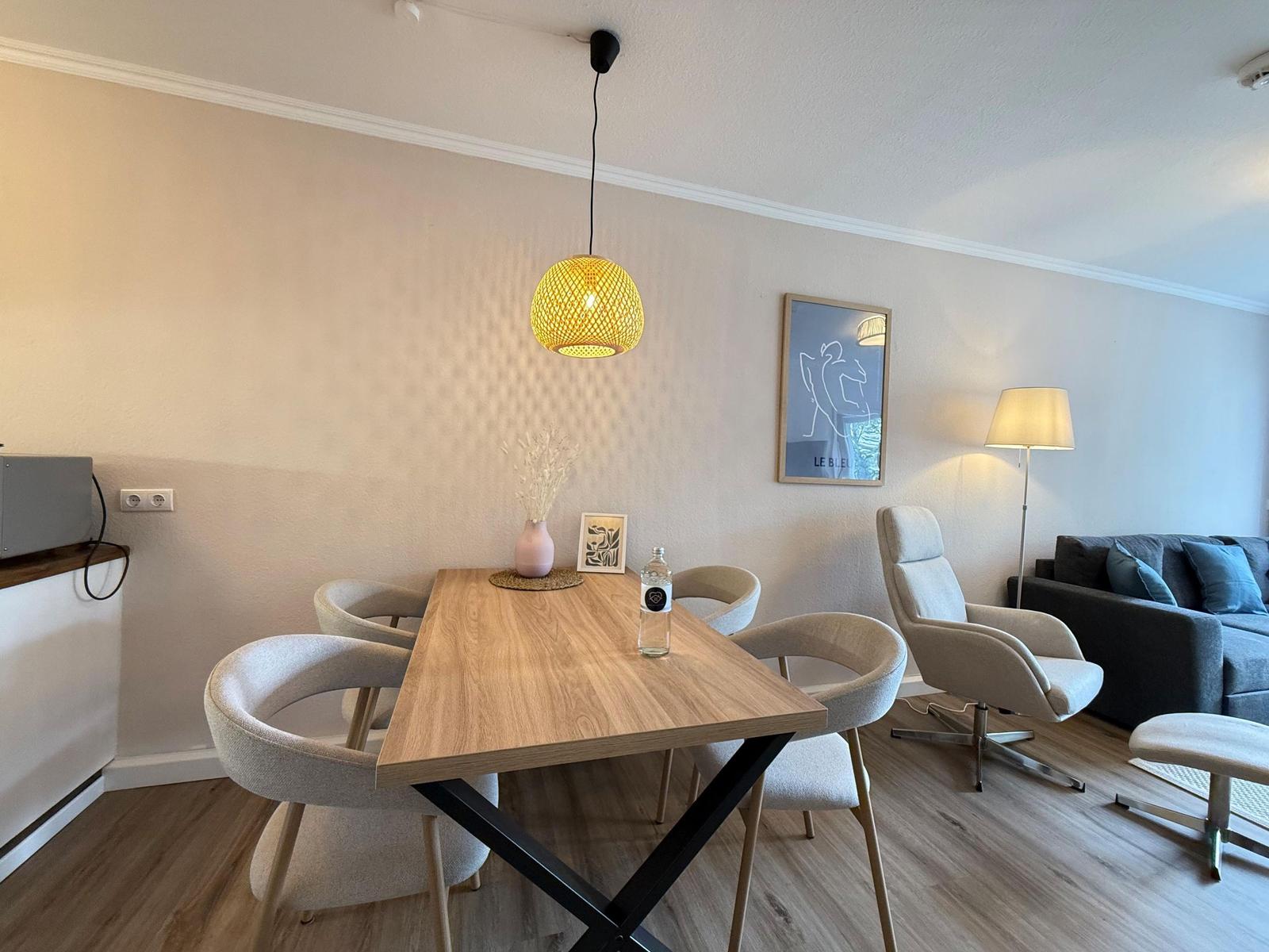 Essbereich mit Holztisch und Stühlen, hängende Lampe und Wohnbereich mit Sofa.
