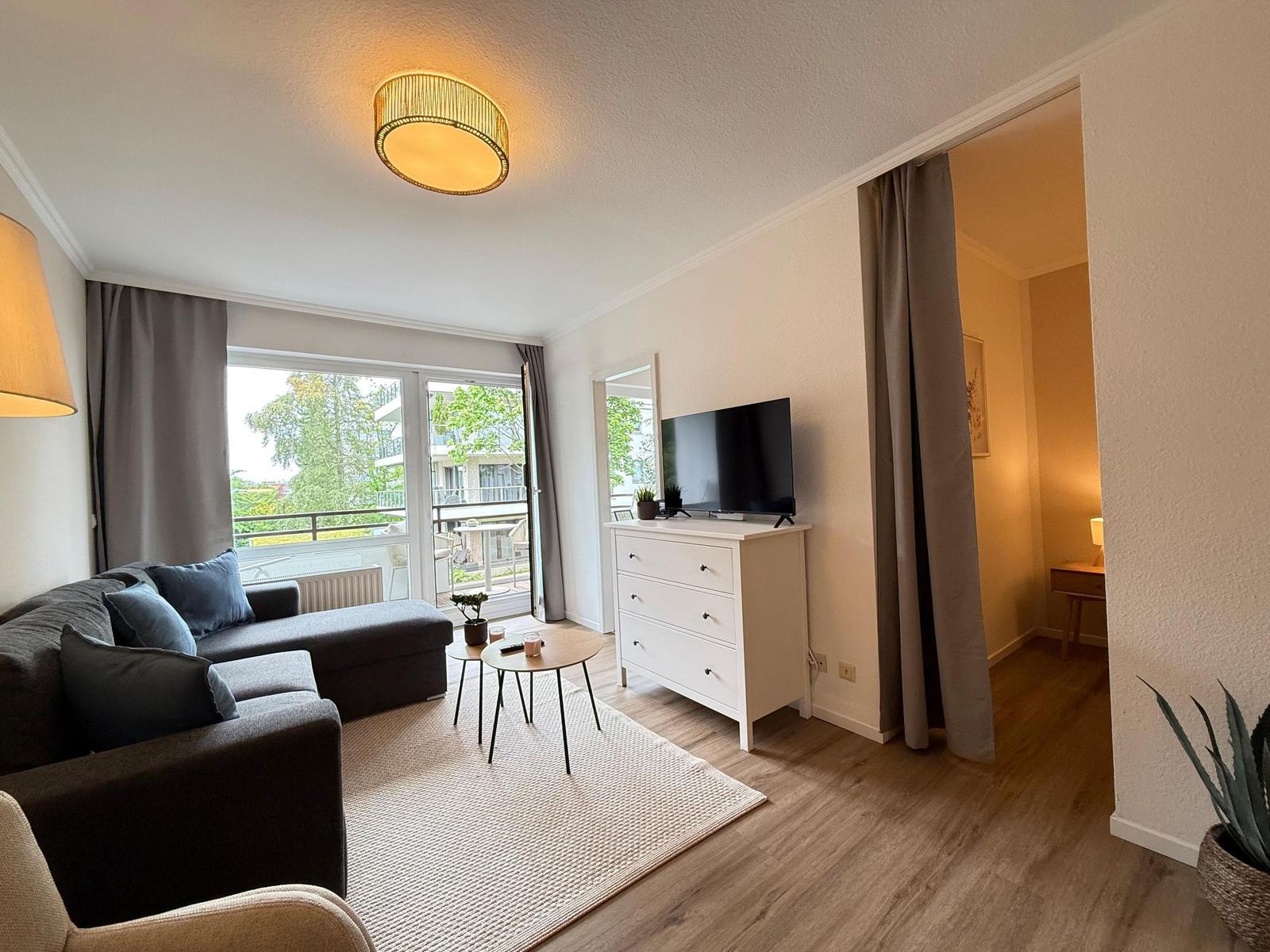 Wohnzimmer mit Sofa, Fernseher und Balkonansicht.