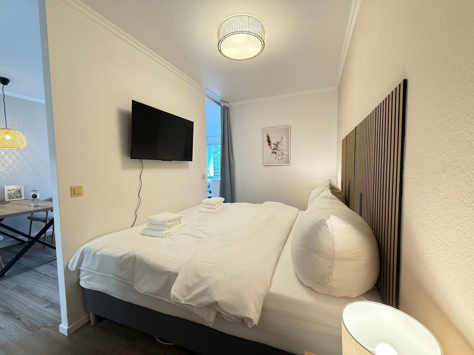 Schlafzimmer mit Bett, Fernseher und Fenster. Holzgestell und Wanddekoration.