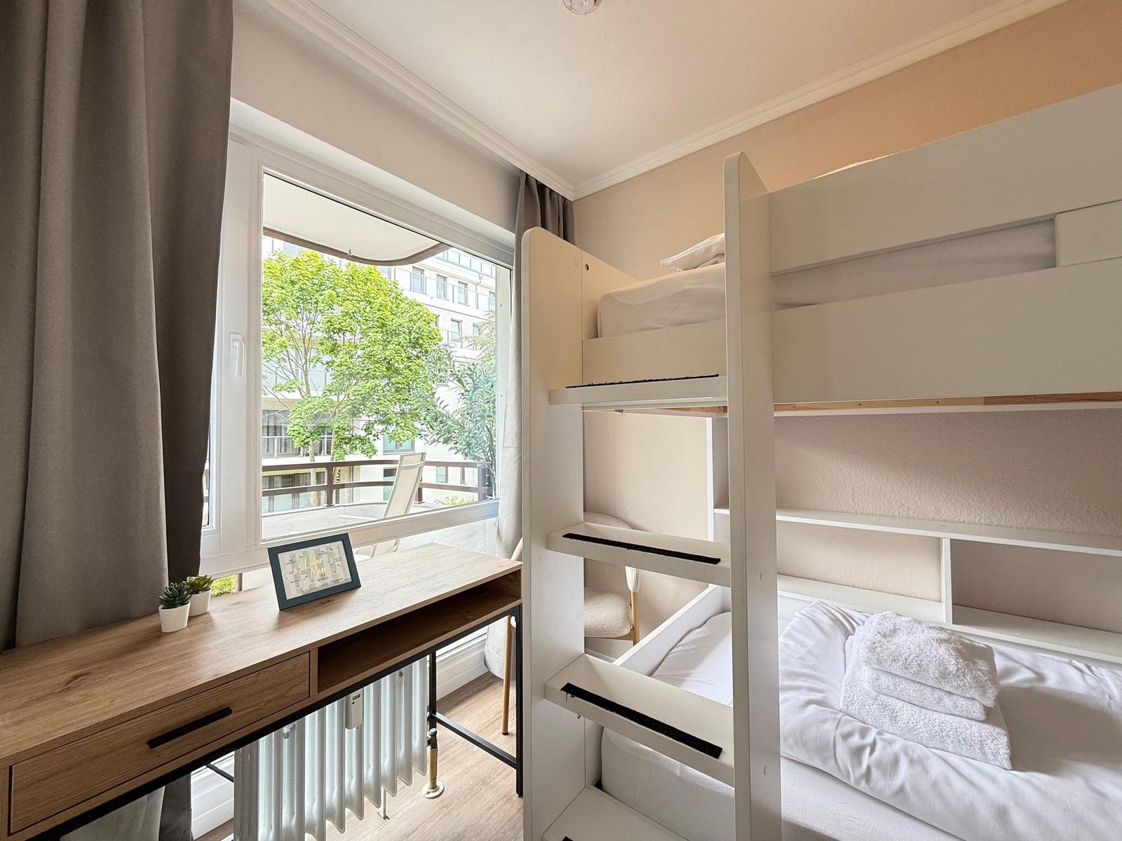 Zimmer mit Doppelstockbett, Schreibtisch und Balkonblick.