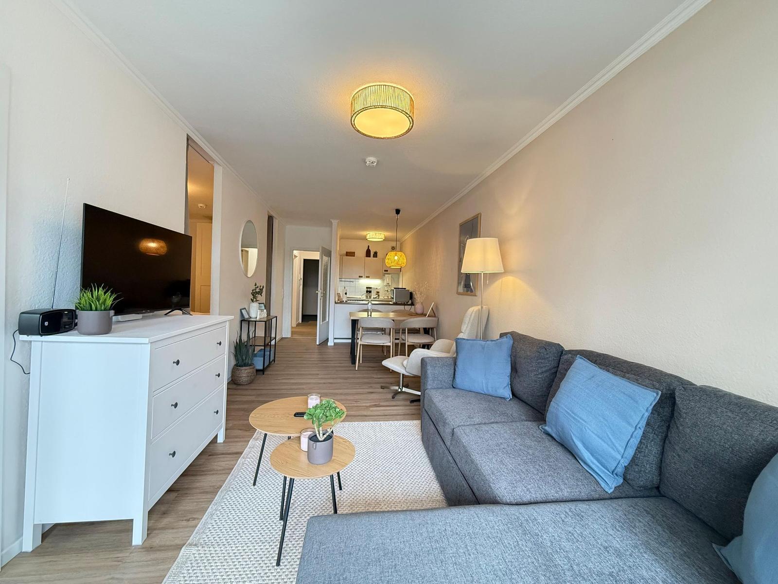 Wohnzimmer mit Sofa, TV und Küchenbereich im Hintergrund.