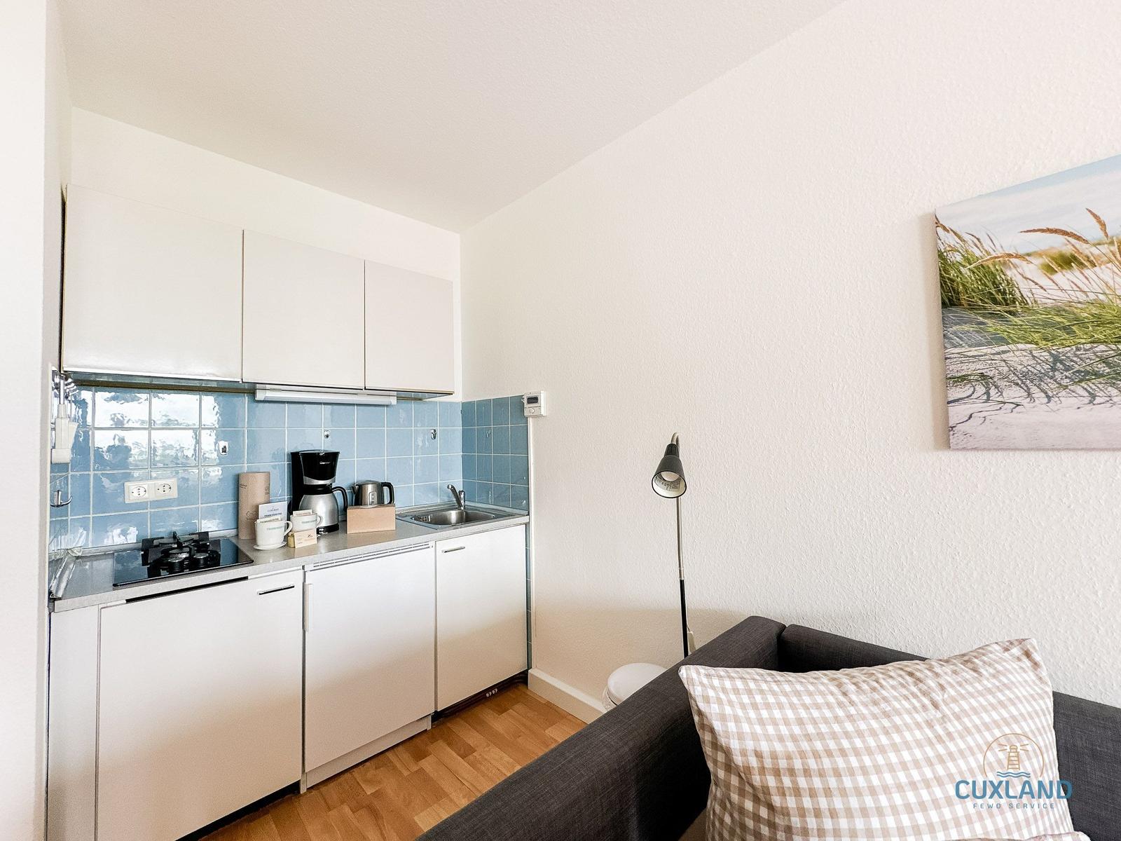 Küche mit weißen Schränken und blauer Fliesenwand. Sofa mit kariertem Kissen.