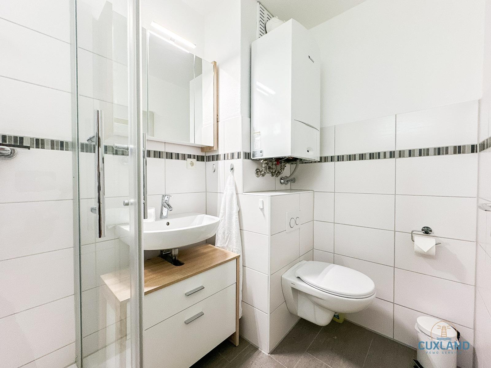 Badezimmer mit Dusche, Waschbecken und WC. Weiße Fliesen und Holzakzente.