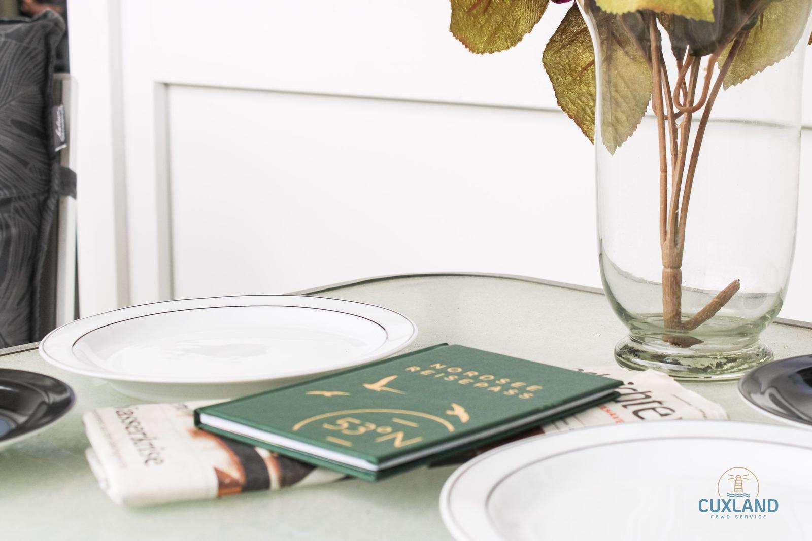 Tisch mit Teller, Reisepass und Blumen im Glas