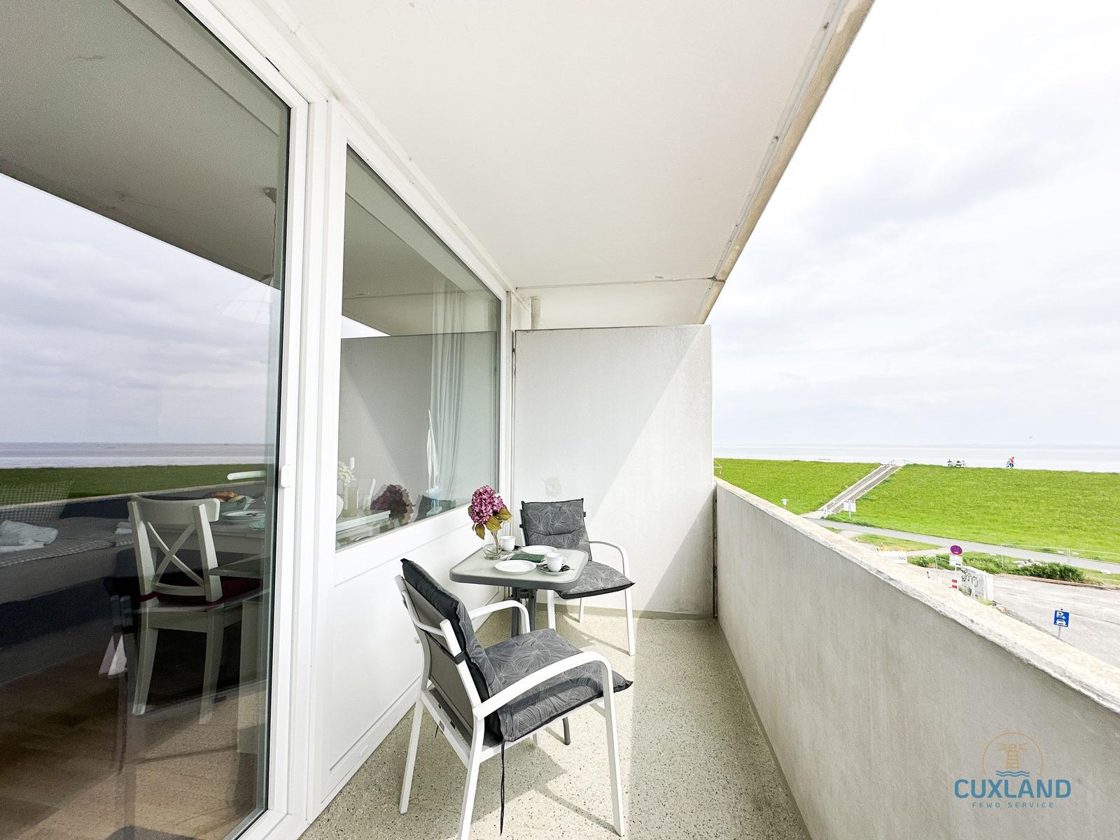 Terrasse mit Tisch und zwei Stühlen, Blick auf Grünfläche und Strand.