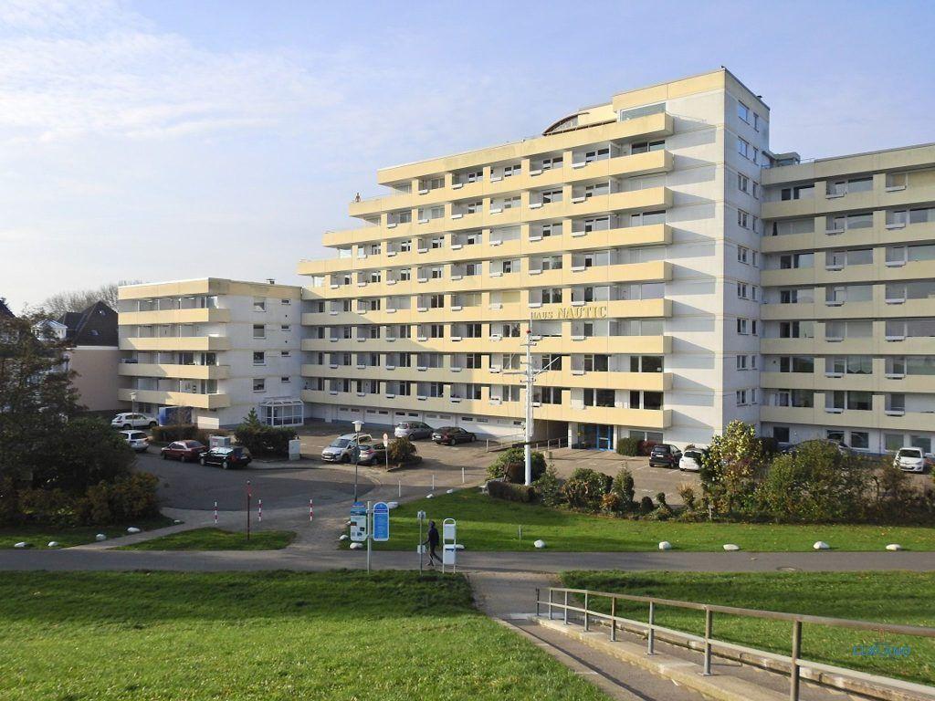 Hochhaus mit mehreren Stockwerken und Balkonen. Parkplatz und Grünflächen vor dem Gebäude.