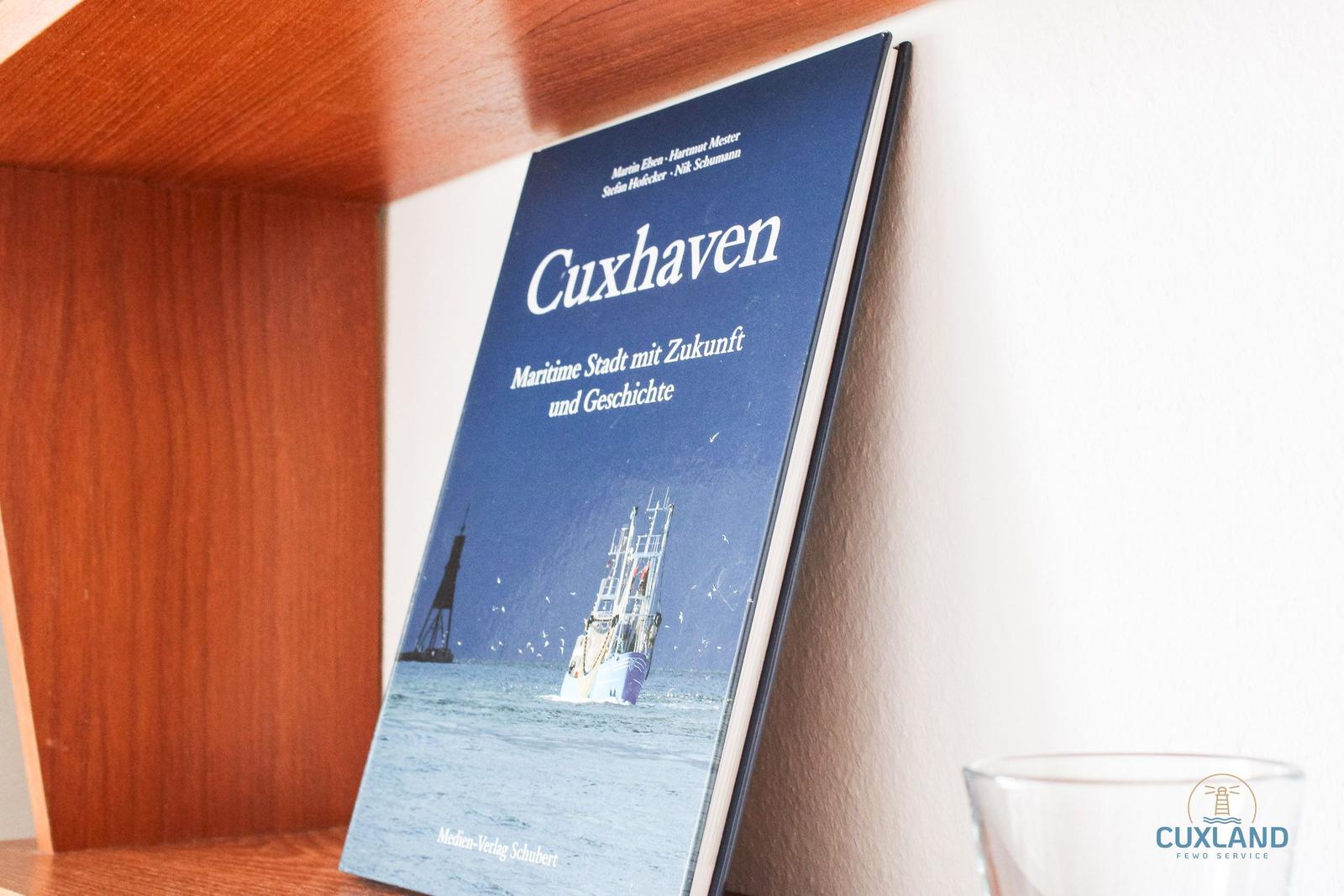 Ein Buch über Cuxhaven steht auf einem Holzregal. Es zeigt ein Schiff und einen Leuchtturm.