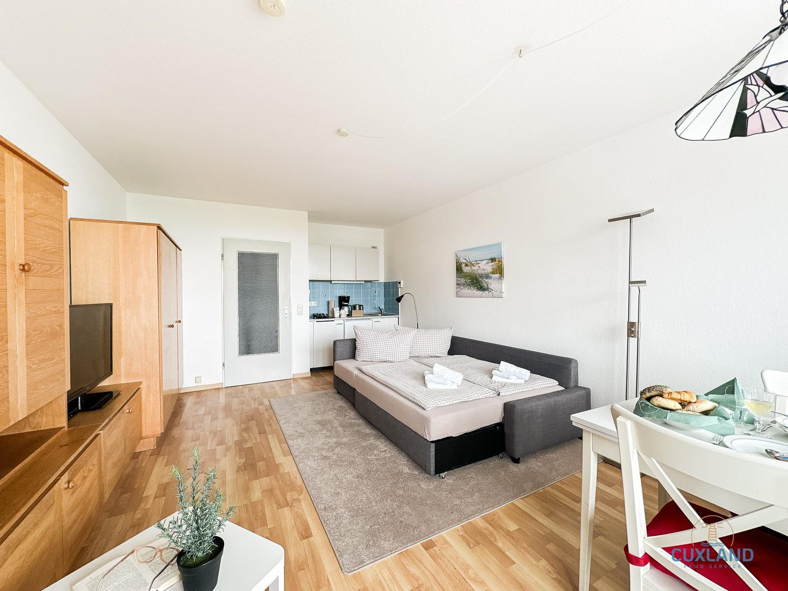 Wohnung mit Schlafsofa, Küche und Essbereich. Holzfußboden und helle Wände.