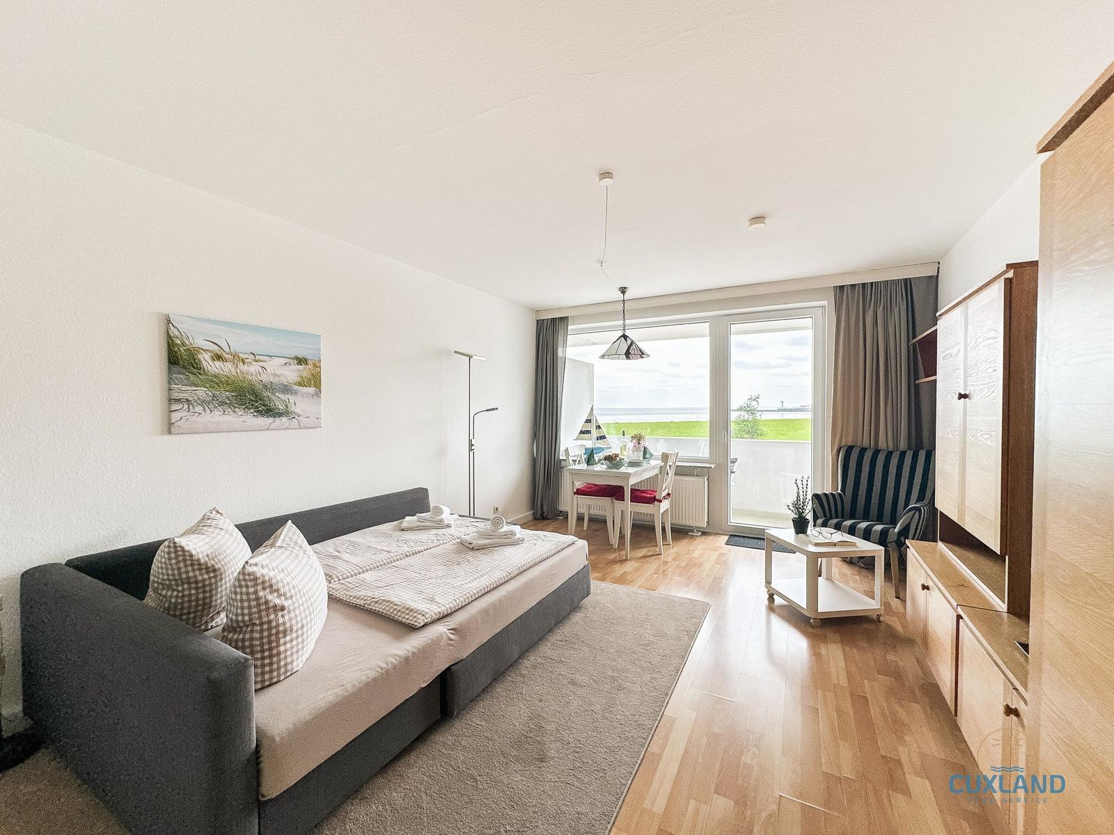 Wohnbereich mit Schlafcouch, Esstisch und Balkon mit Meerblick.
