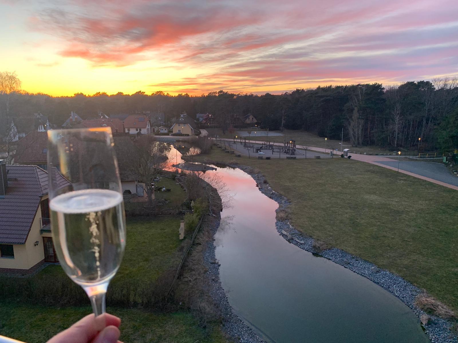 Ein Glas Champagner genießt man bei Sonnenuntergang über einen Fluss und Grünflächen.