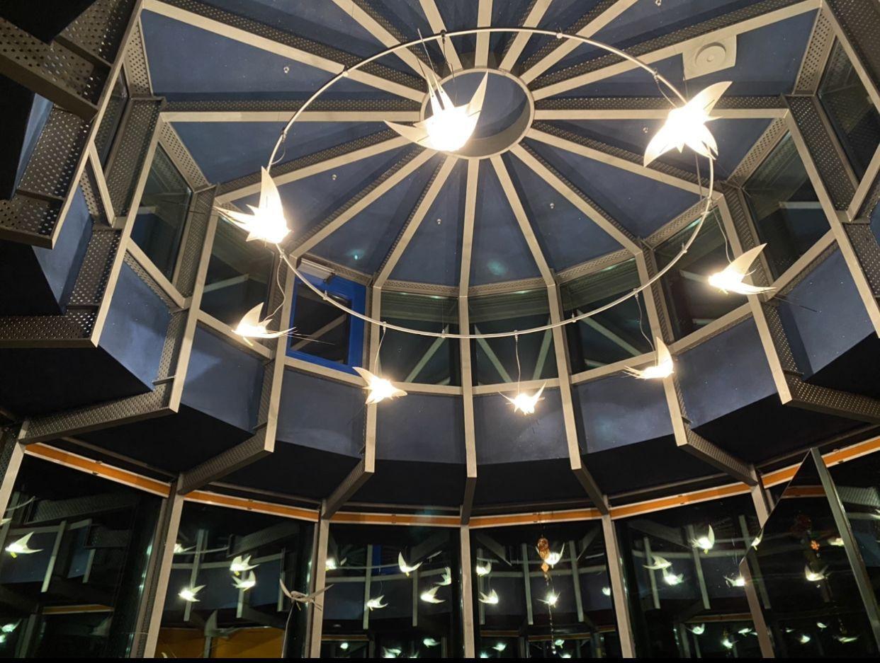 Decke mit geometrischem Design und hängenden Lichtern in Form von Vögeln.