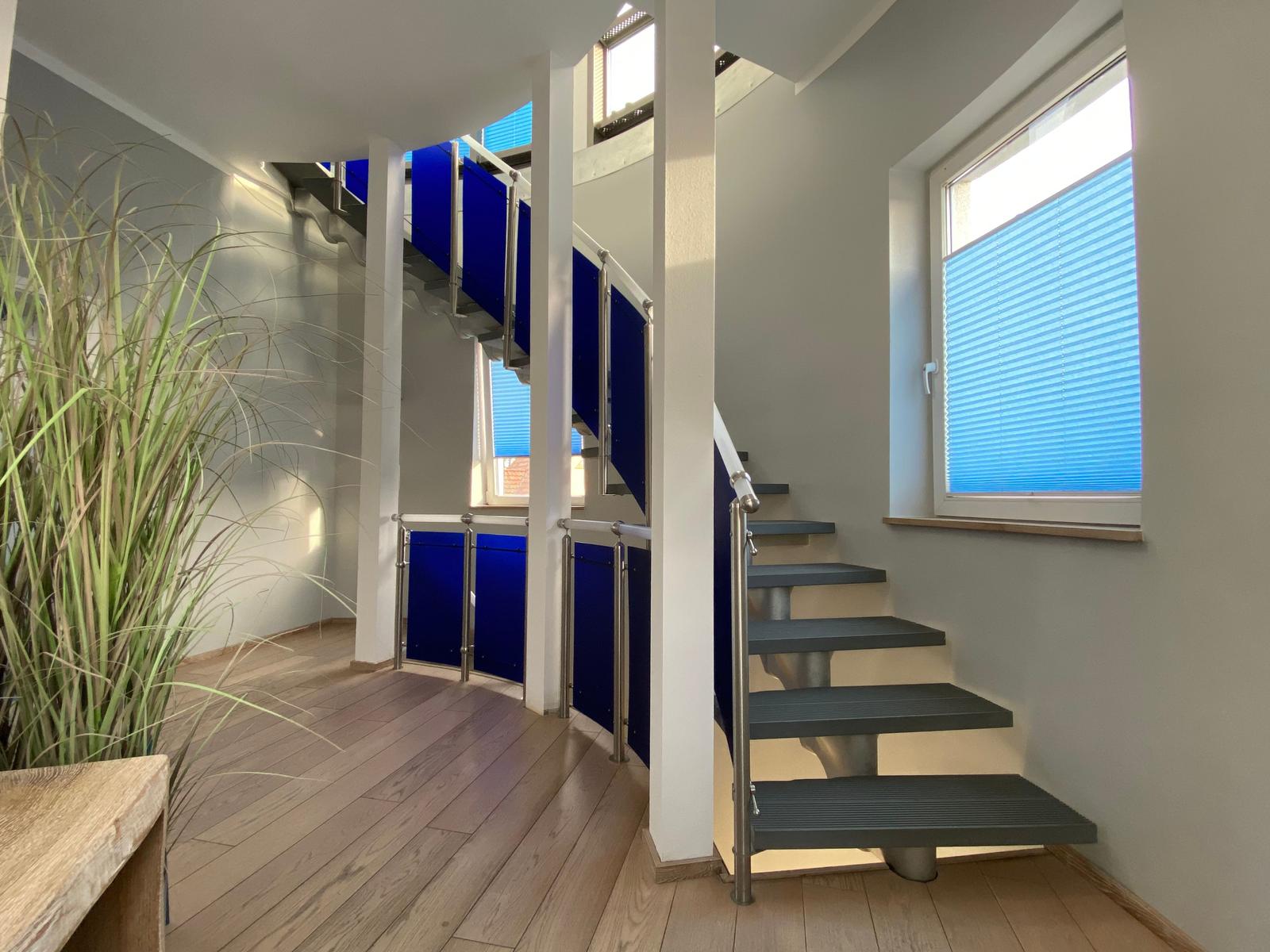 Treppe mit blauen Geländern und Holzboden. Fenster mit Jalousien.