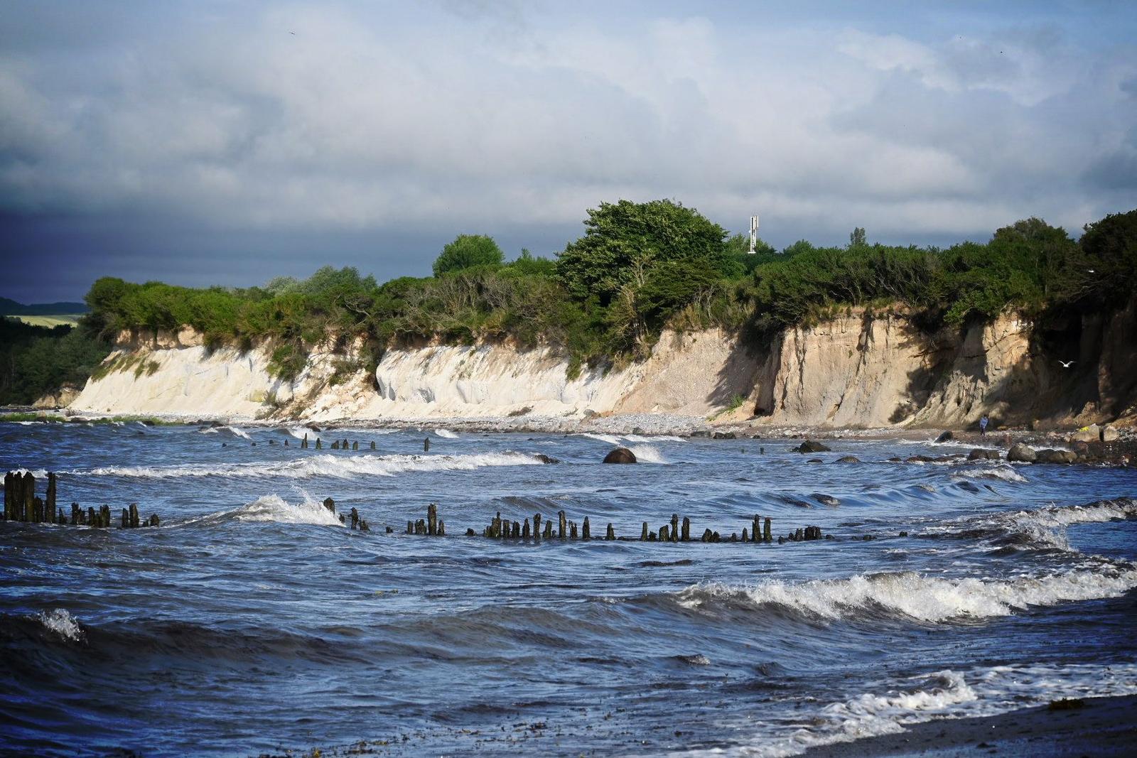 Meer mit Wellen, Felsen und Küstenhängen mit Bäumen.