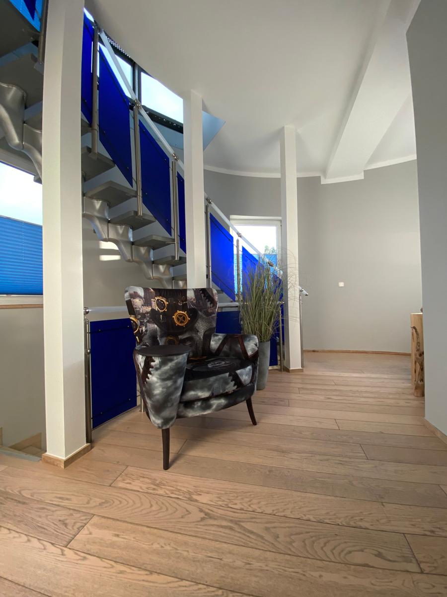 Eingangsbereich mit Sitzgelegenheit, Holzboden und blauer Treppe.