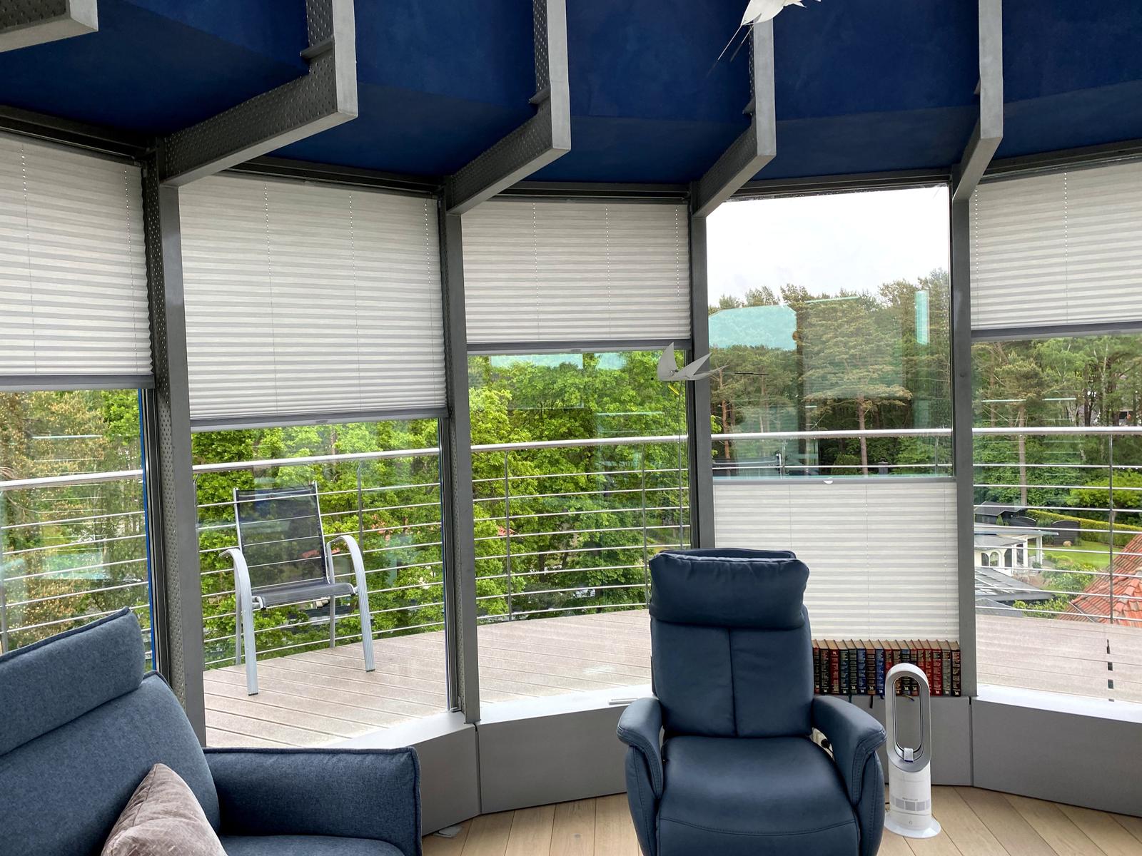 Raum mit blauem Sessel und Sofa, Blick auf Balkon mit Garten